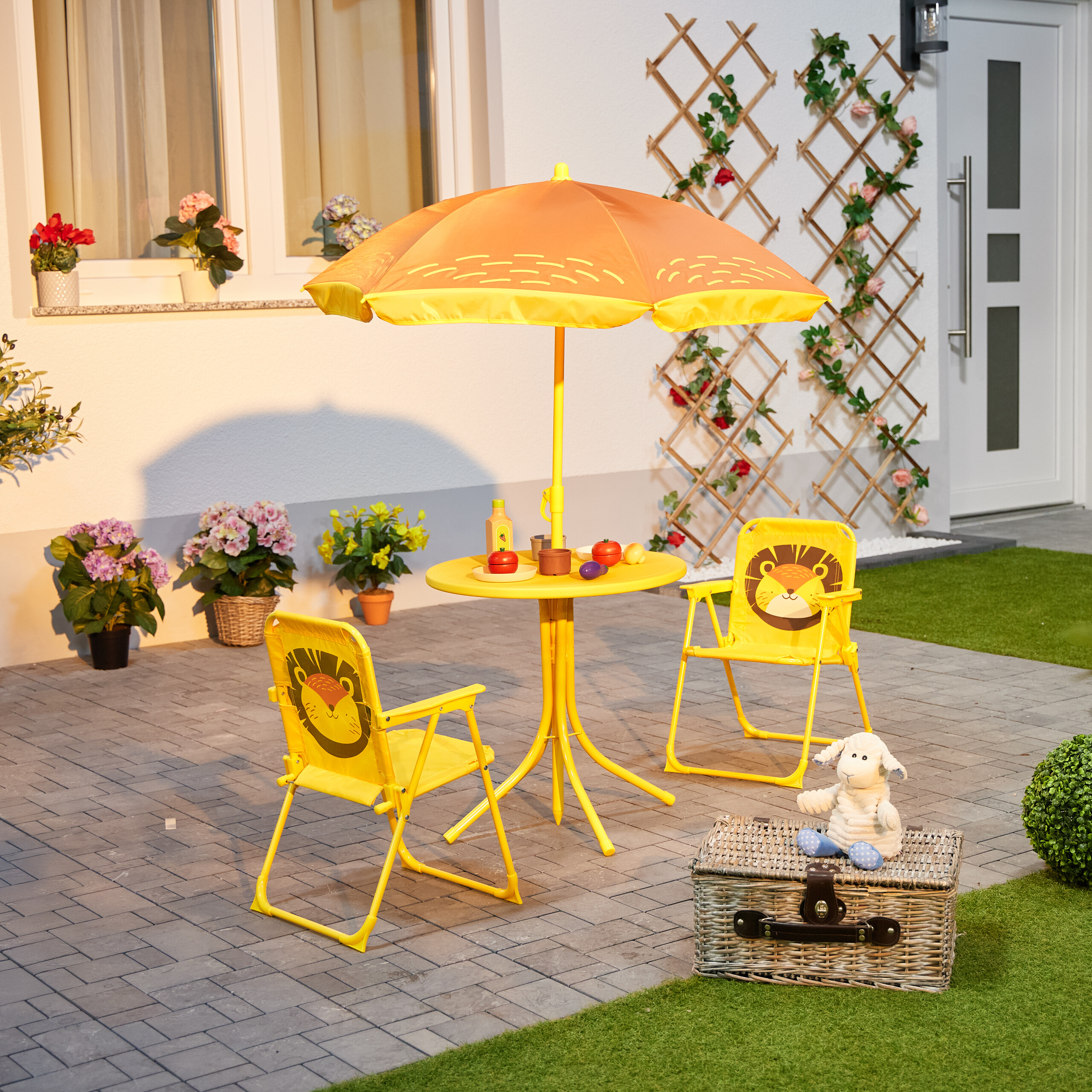 Ein gelbes Gartenset mit Sonnenschirm, zwei Löwenstühlen, Tisch mit Spielzeug und Plüschschaf auf Korb.