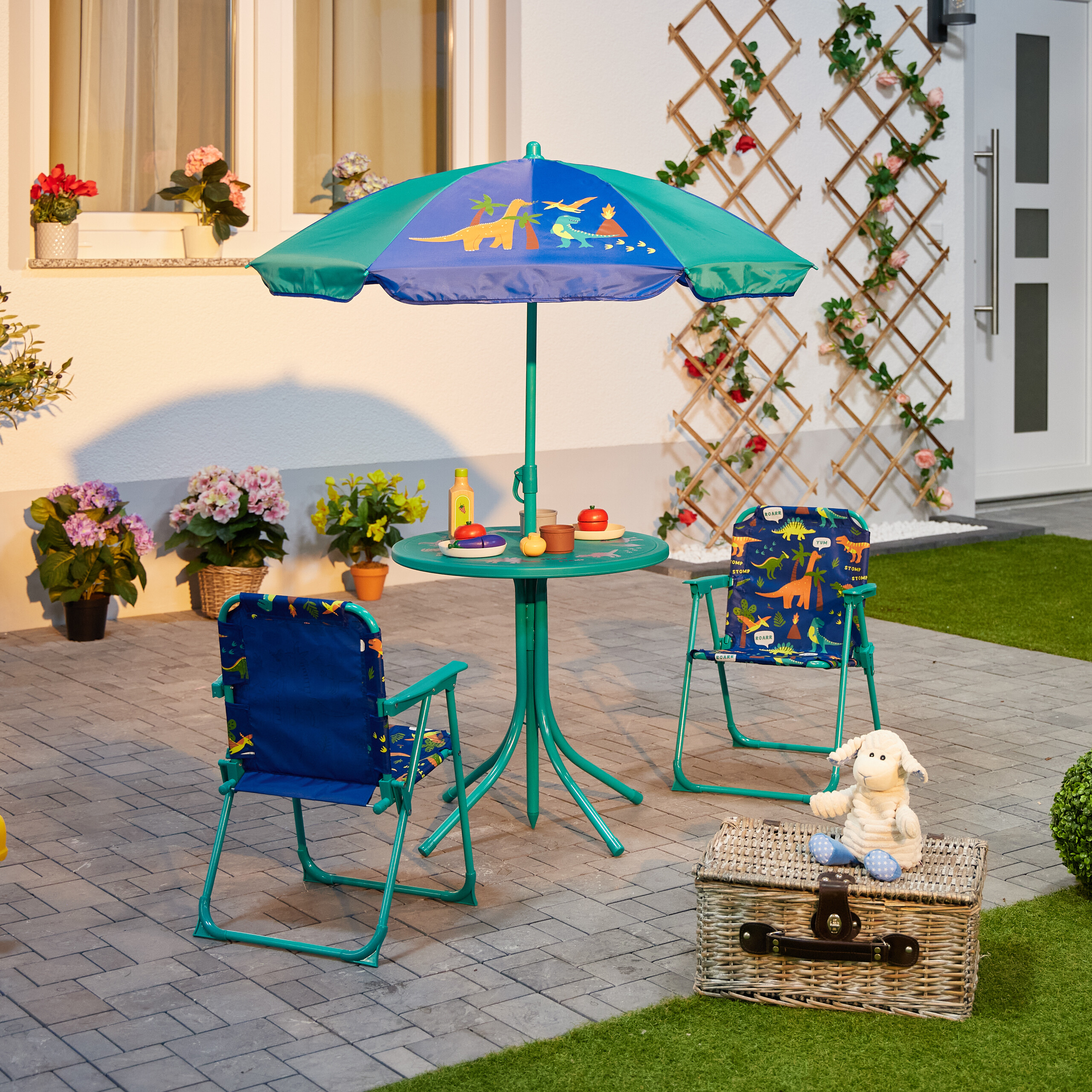 Kinderspieltisch mit bunten Dinosauriern, zwei Stühlen und einem Regenschirm im Garten auf Pflastersteinen.