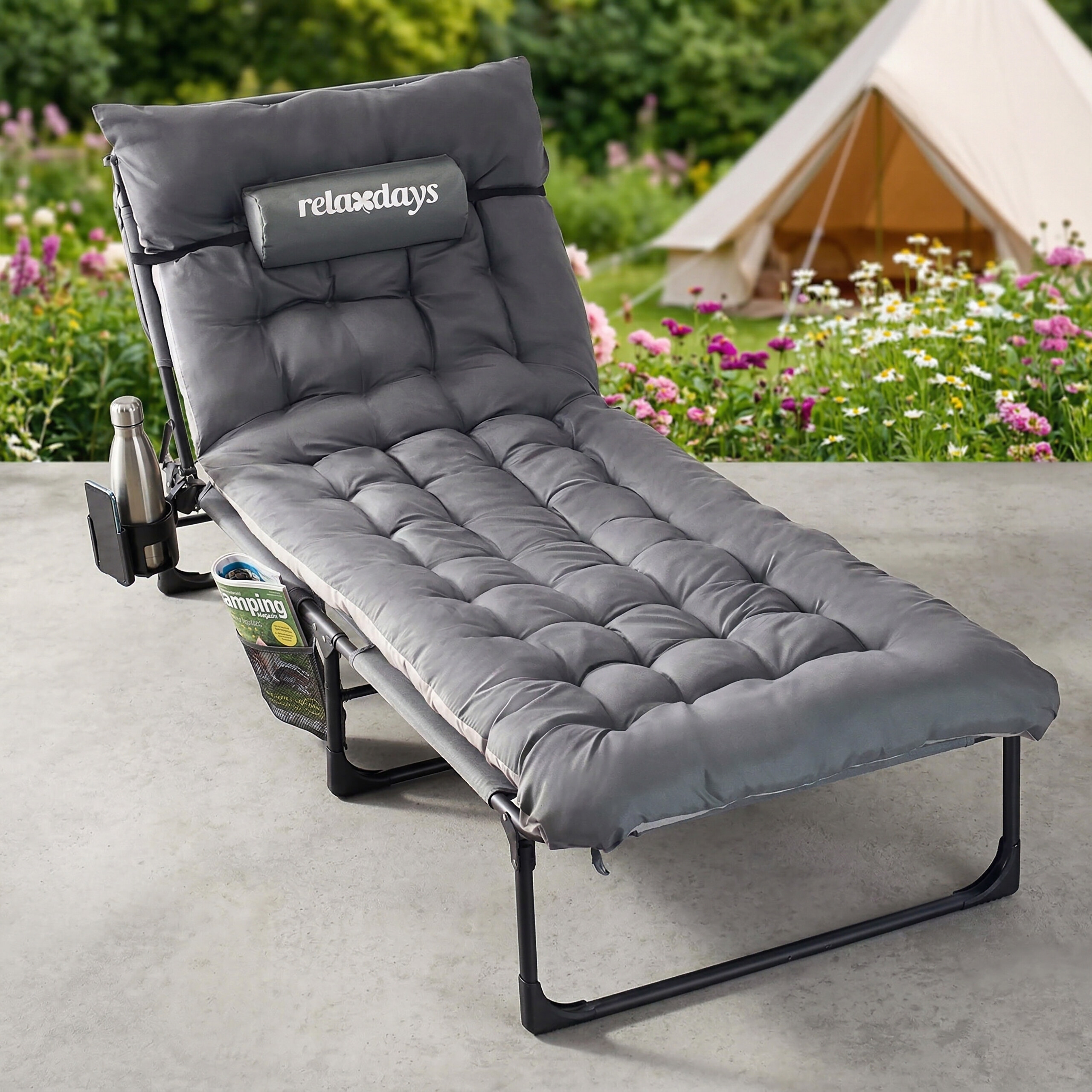 Eine graue Relaxliege mit dickem Polster, Flaschenhalter und Magazintasche steht auf einer Terrasse vor einem Zelt.