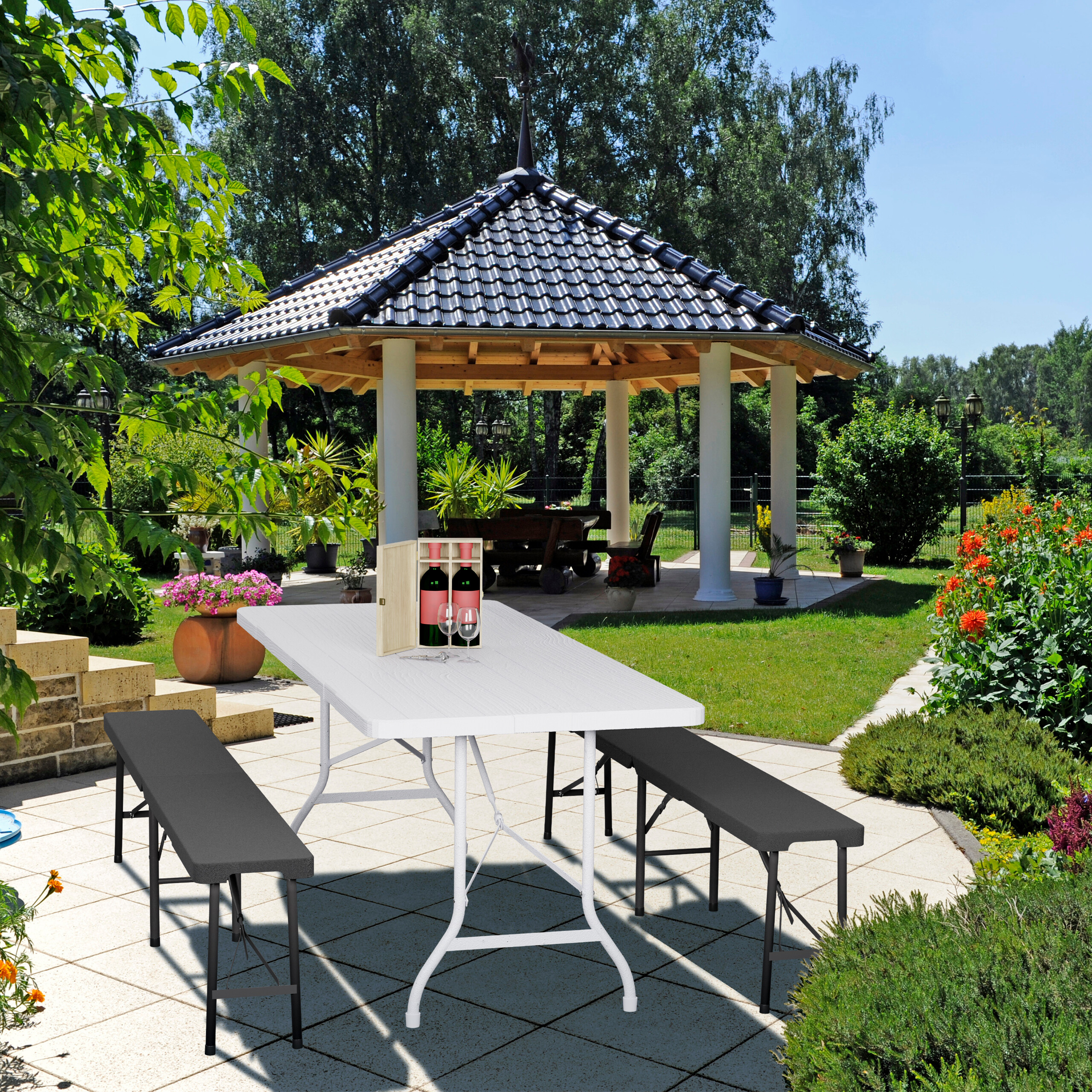 Ein weißer Tisch mit zwei Bänken steht auf einer Terrasse im Garten, mit einem Holzpavillon im Hintergrund.