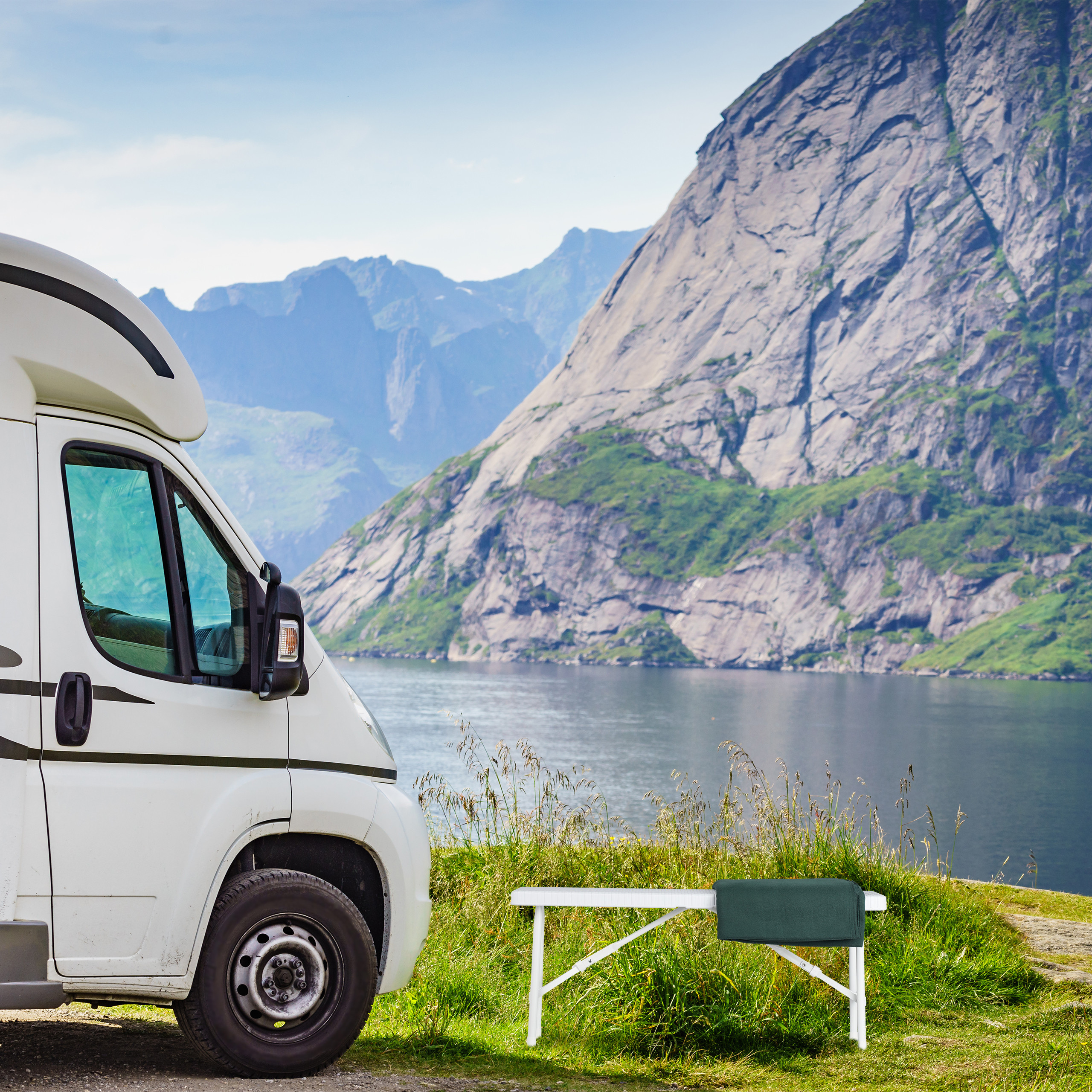 Ein weißes Wohnmobil steht an einem Fjord vor steilen Bergen und Wasser.