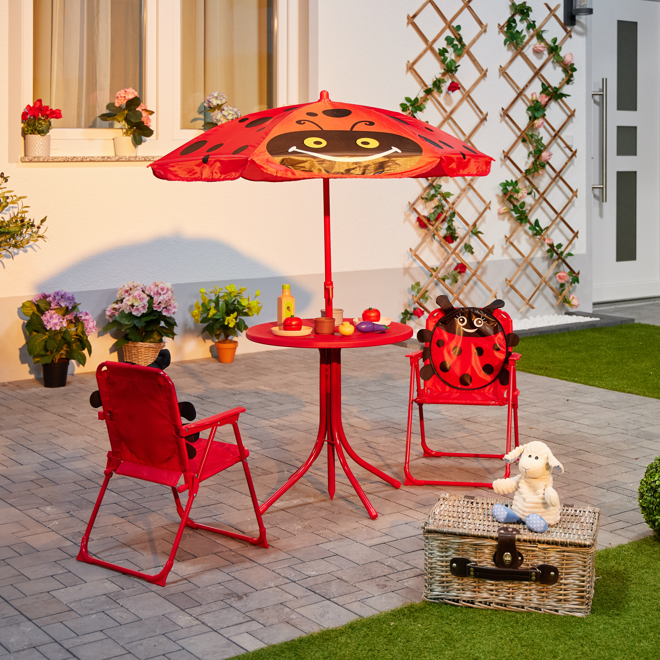 Kindermöbelset in Rot mit Marienkäfer-Sonnenschirm und -Stuhl, Korb und Stoffschaf auf der Terrasse.
