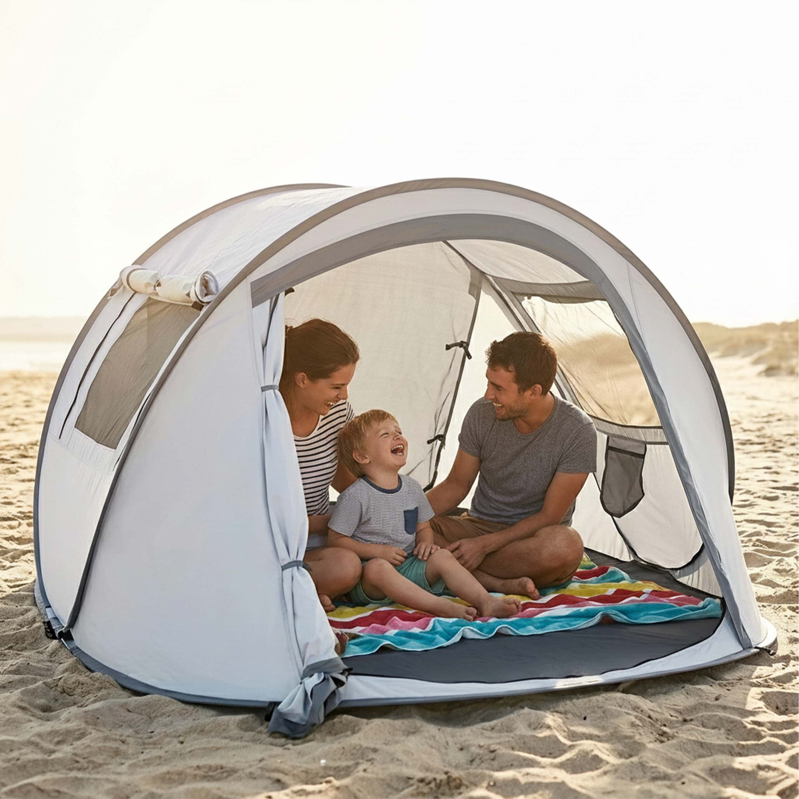 Eine Familie mit einem Kind sitzt glücklich in einem Pop-up-Strandzelt auf sandigem Boden am Strand.