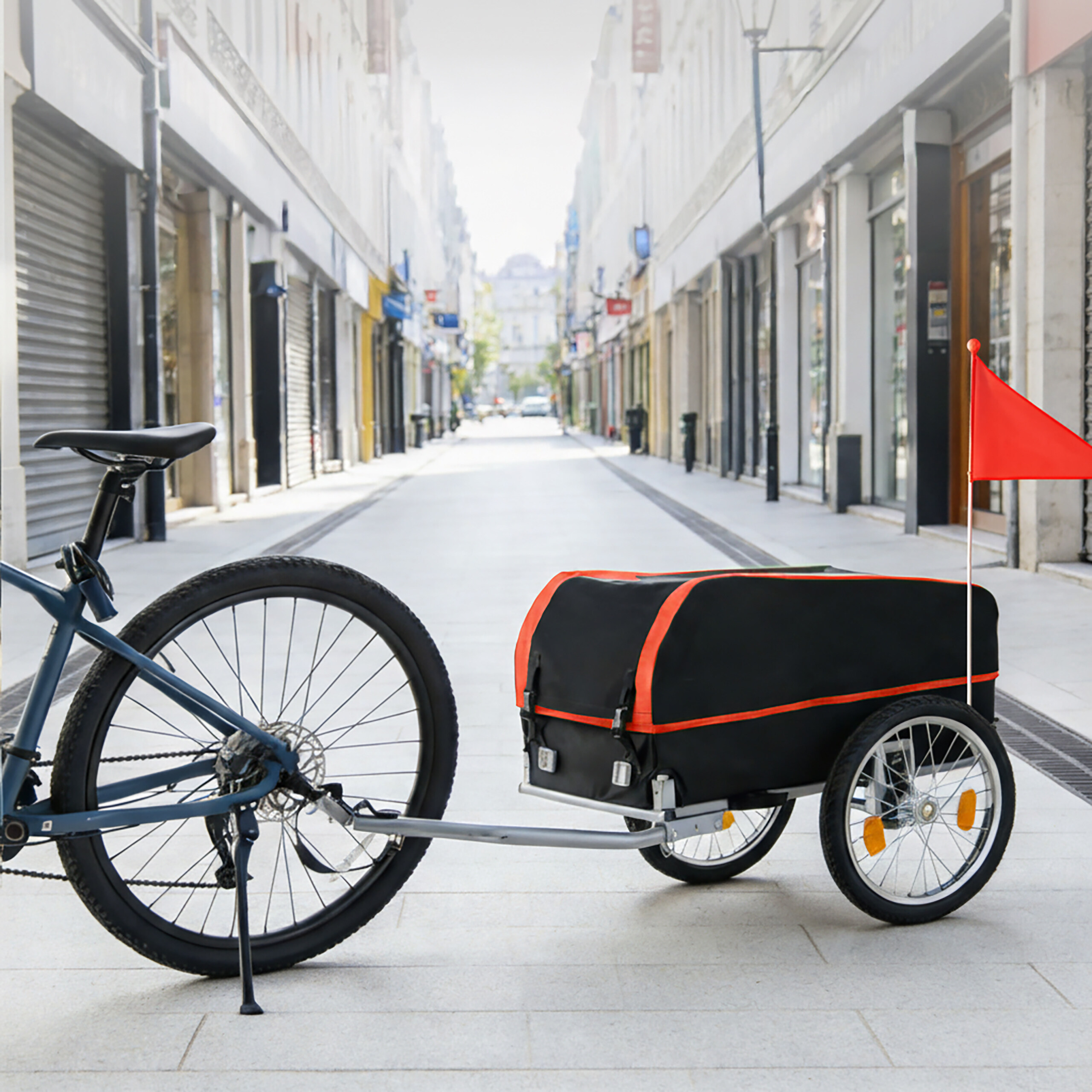 Ein blaues Fahrrad mit Anhänger und roter Fahne parkt in einer Fußgängerzone.