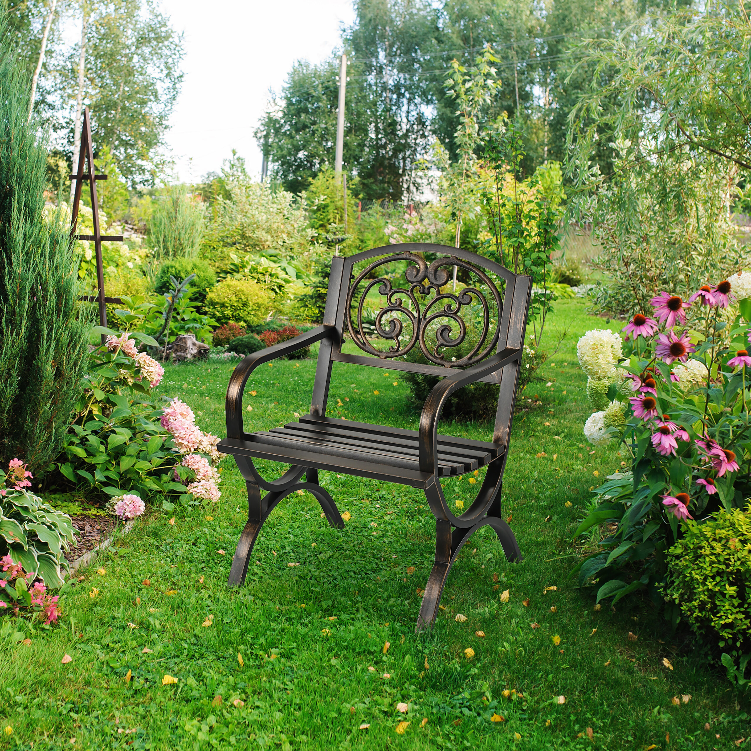 Eine schwarze Gartenbank steht auf einer grünen Wiese, umgeben von bunten Blumen und Sträuchern.