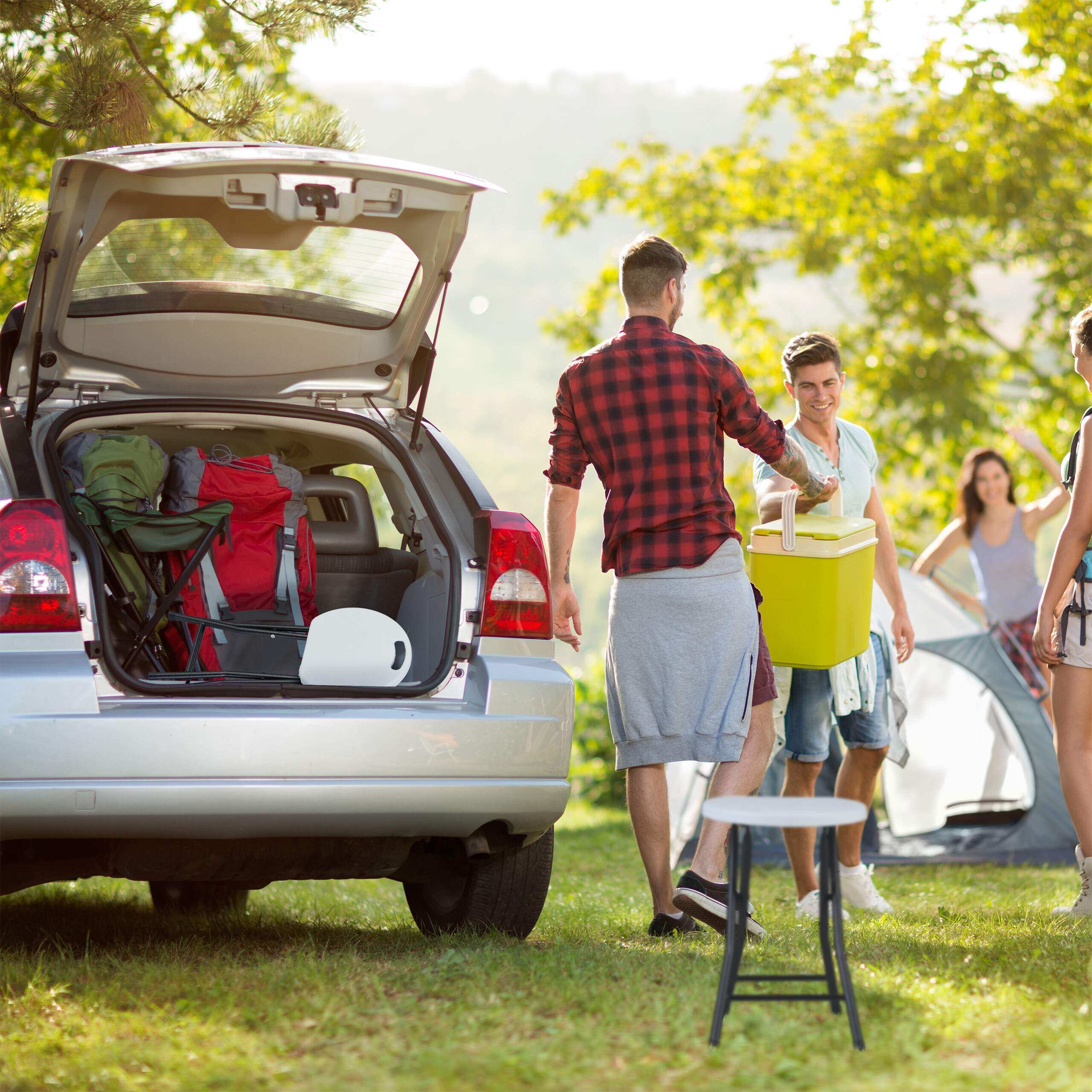 Freunde beim Camping: Ein Mann lädt Ausrüstung aus dem offenen Kofferraum eines Autos.