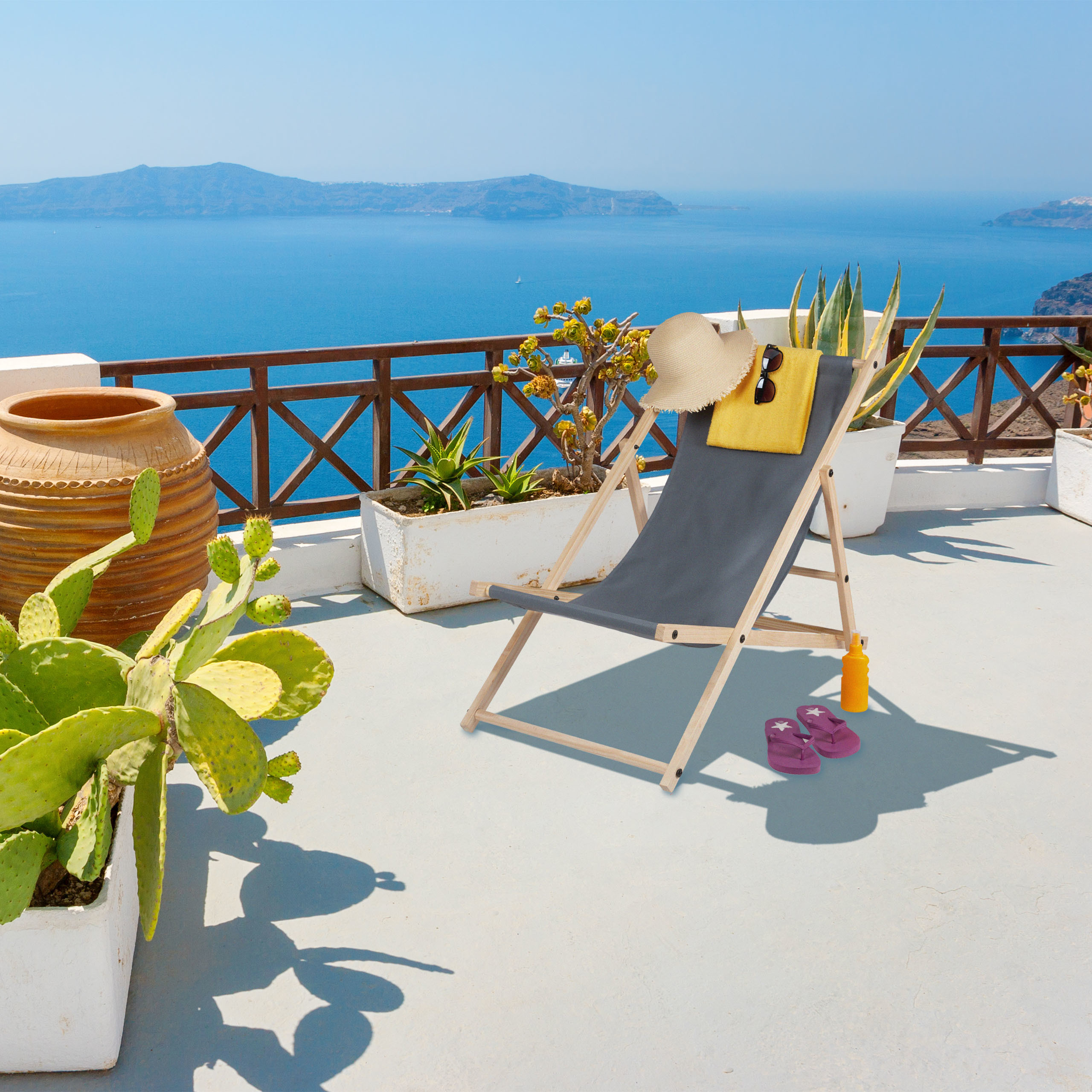 Ein Liegestuhl mit Hut und Handtuch auf einer sonnigen Terrasse mit Meerblick, Topfkakteen und großem Tontopf.