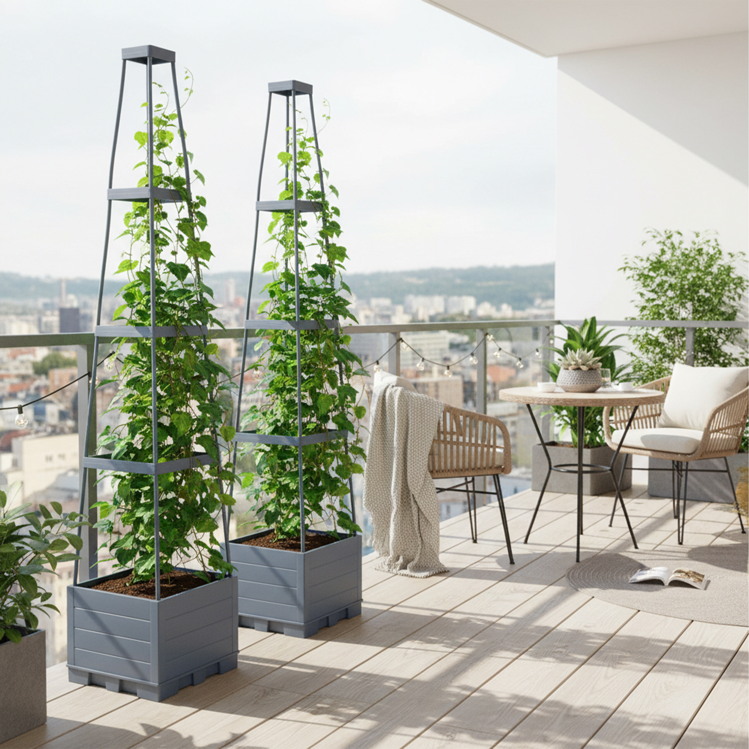 Zwei hohe graue Pflanzkübel mit Kletterpflanzen auf einem sonnigen Balkon mit Stadtblick, Korbstühlen und Tisch.