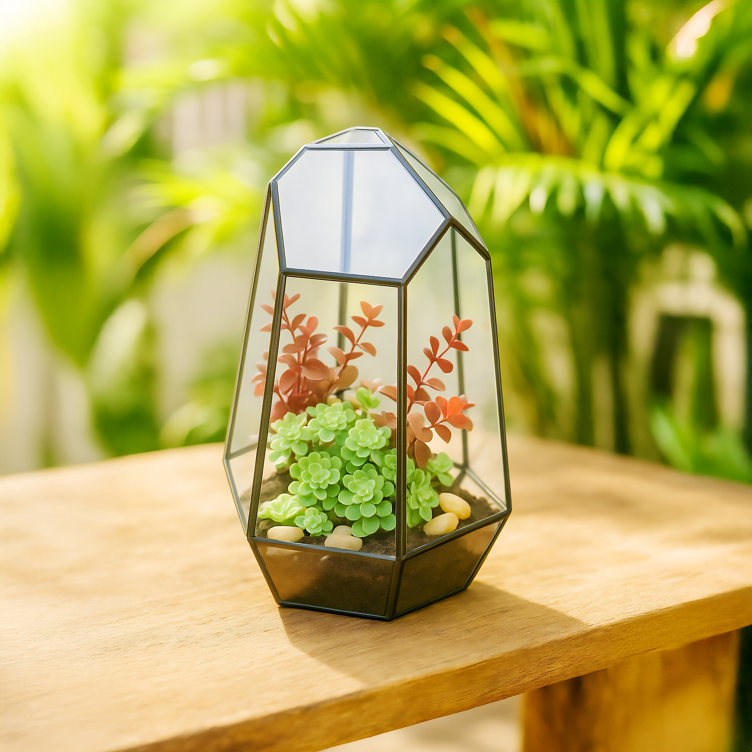 Ein geometrisches Glasterrarium mit grünen Sukkulenten und rötlichen Blättern steht im Freien auf einem Holztisch.