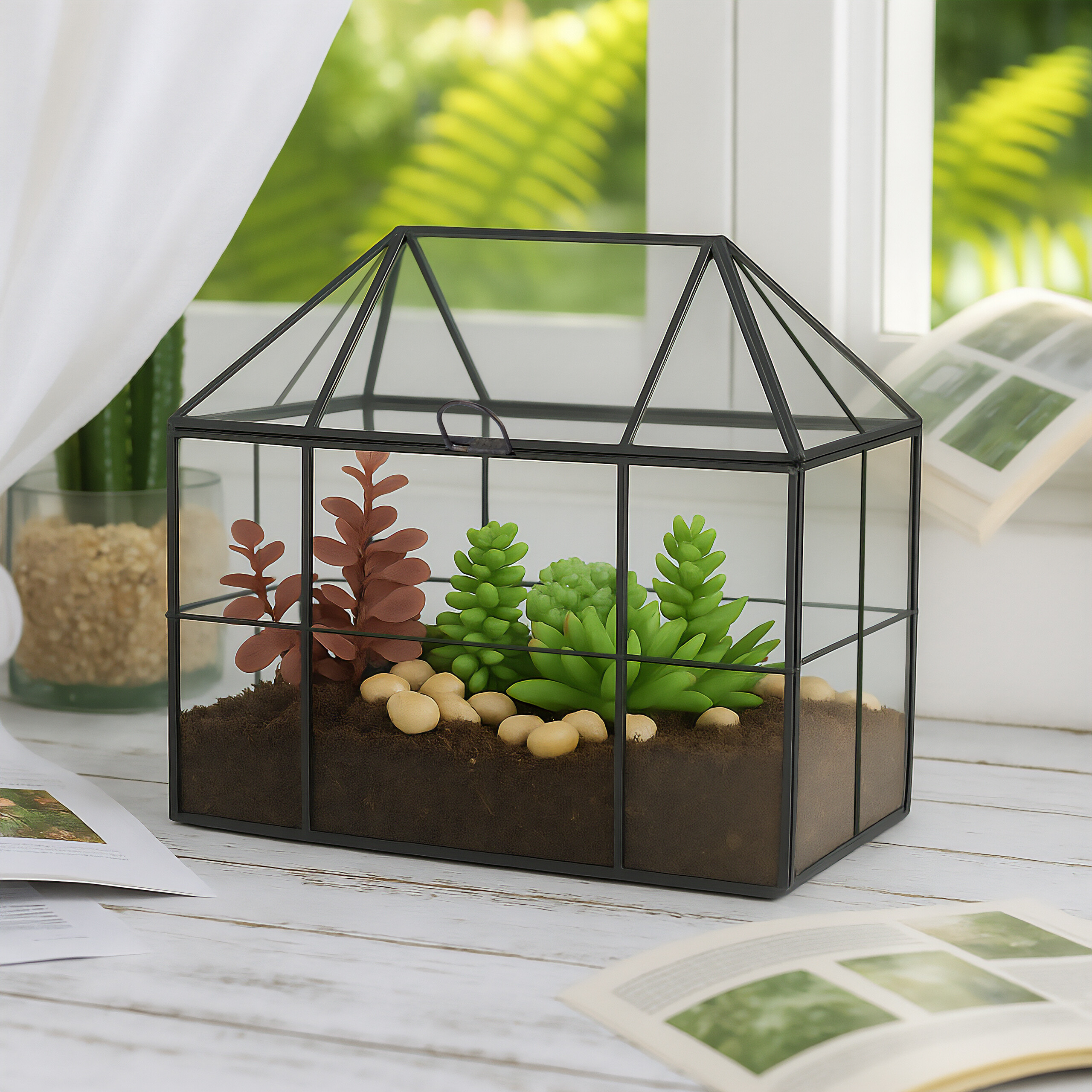 Ein Terrarium aus Glas mit Sukkulenten und Erde auf einem weißen Holztisch am Fenster.