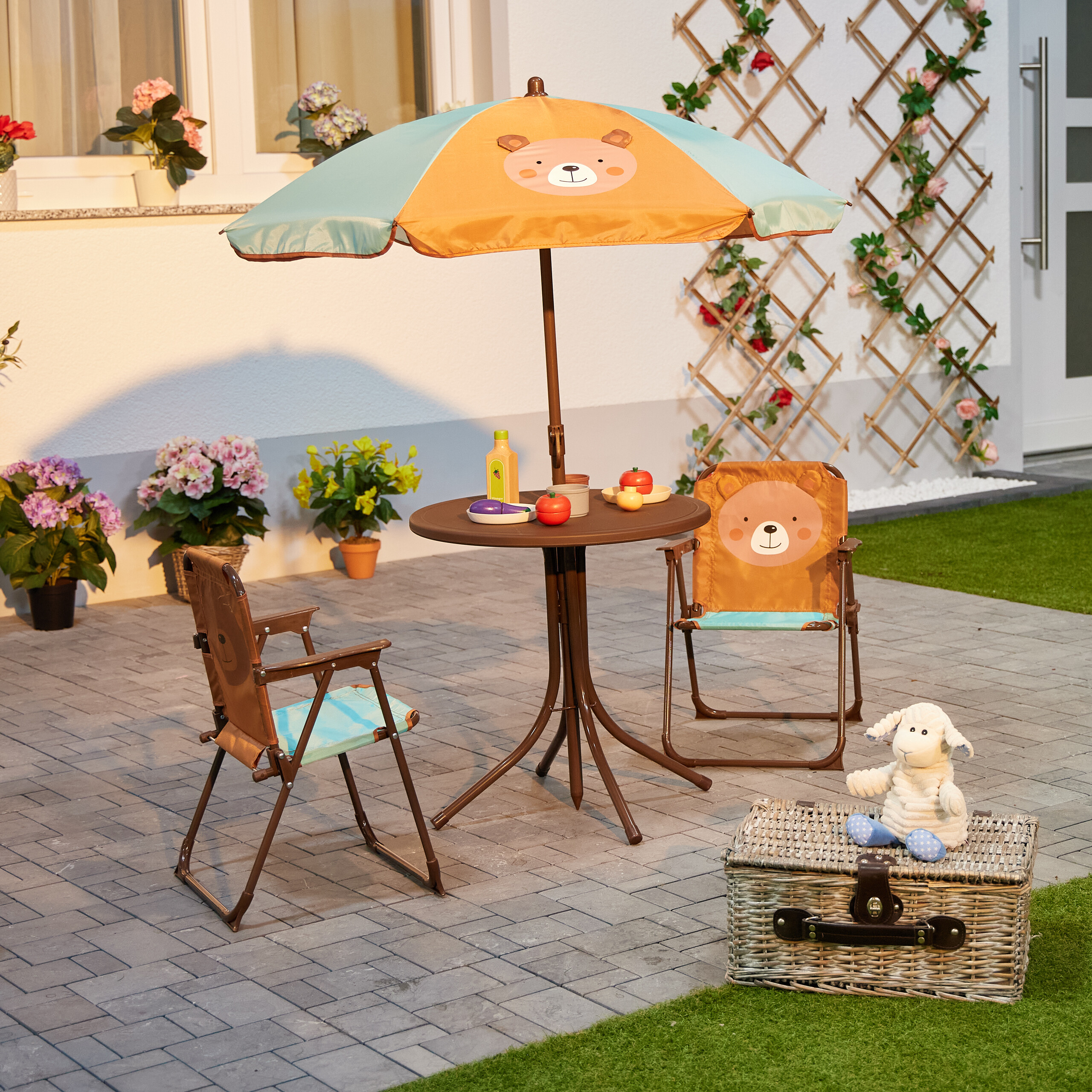 Kindermöbelset mit Bären-Sonnenschirm, Tisch mit Spielzeug, zwei Stühlen und Plüschschaf auf Weidenkorb.