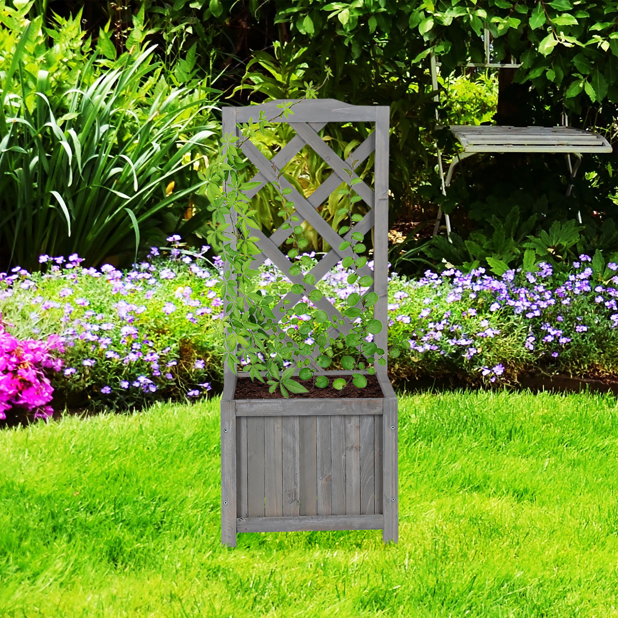 Ein grauer Holzpflanzer mit Rankgitter steht auf einem grünen Rasen in einem Garten mit lila Blumen.