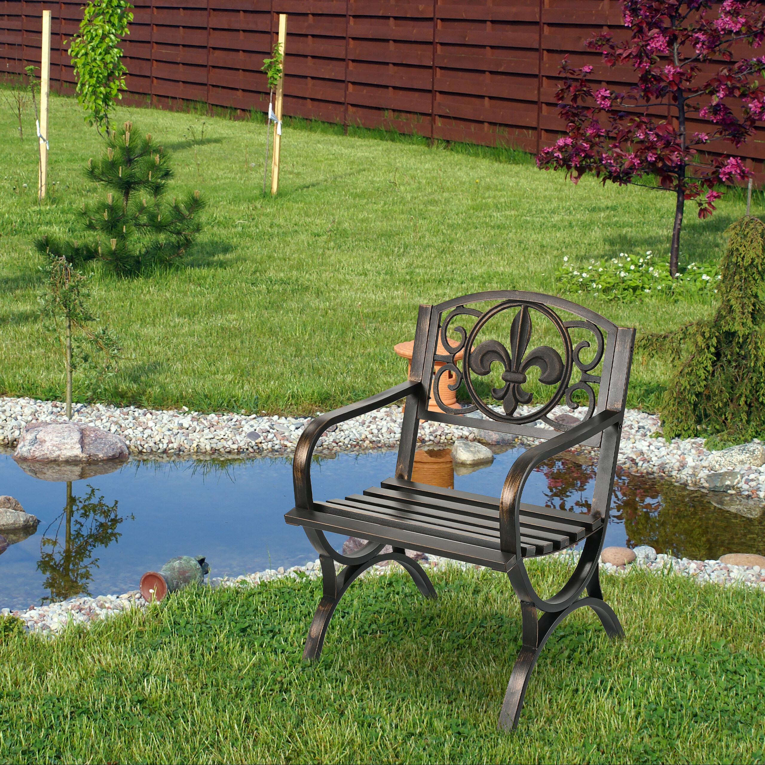 Ein Gartenstuhl aus Metall mit Fleur-de-Lis-Rückenlehne steht auf Rasen neben einem Teich.