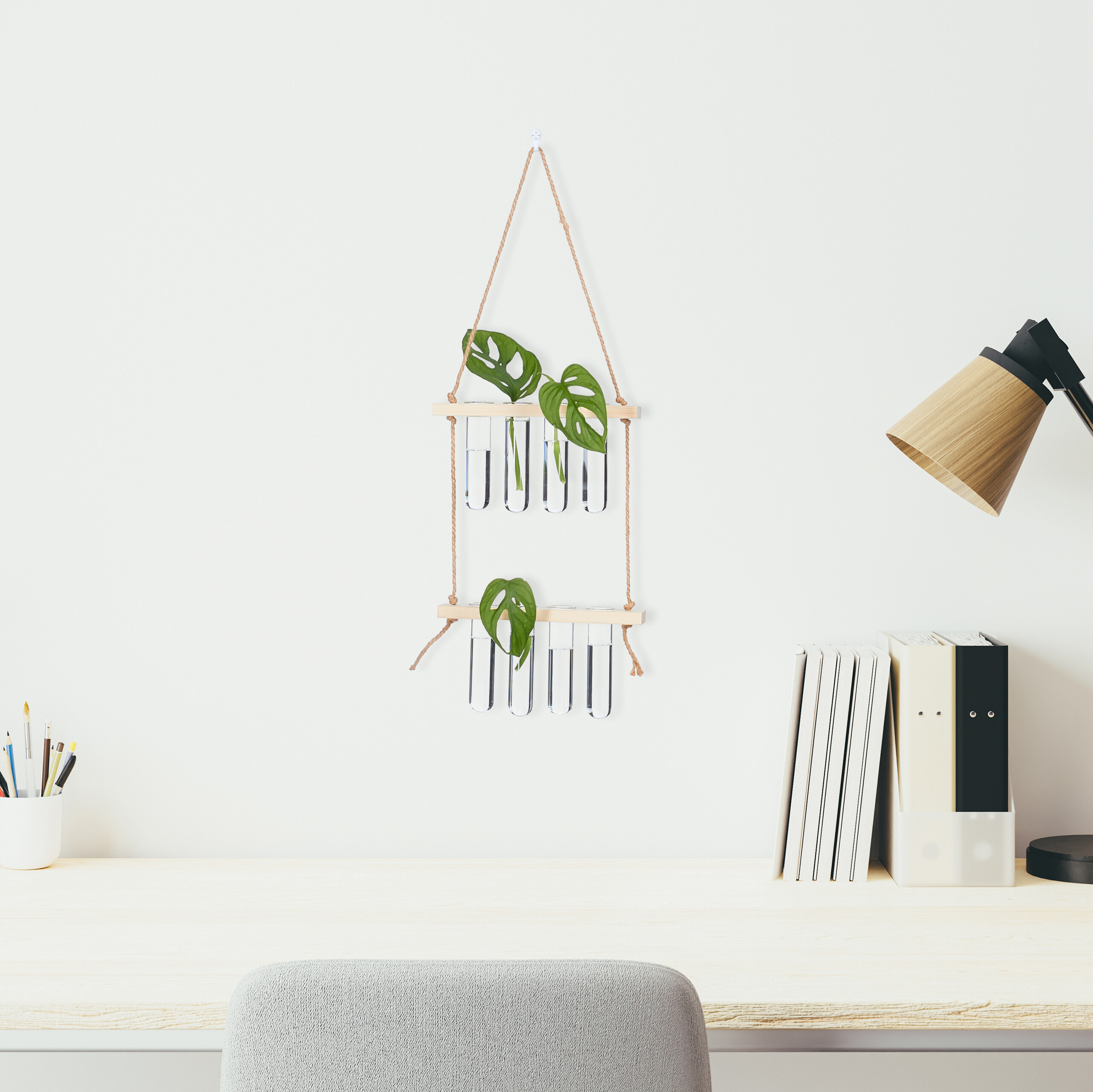 Ein Holztisch zeigt eine hängende Reagenzglas-Pflanze, eine Lampe, Hefte, Stiftehalter und einen grauen Stuhl.