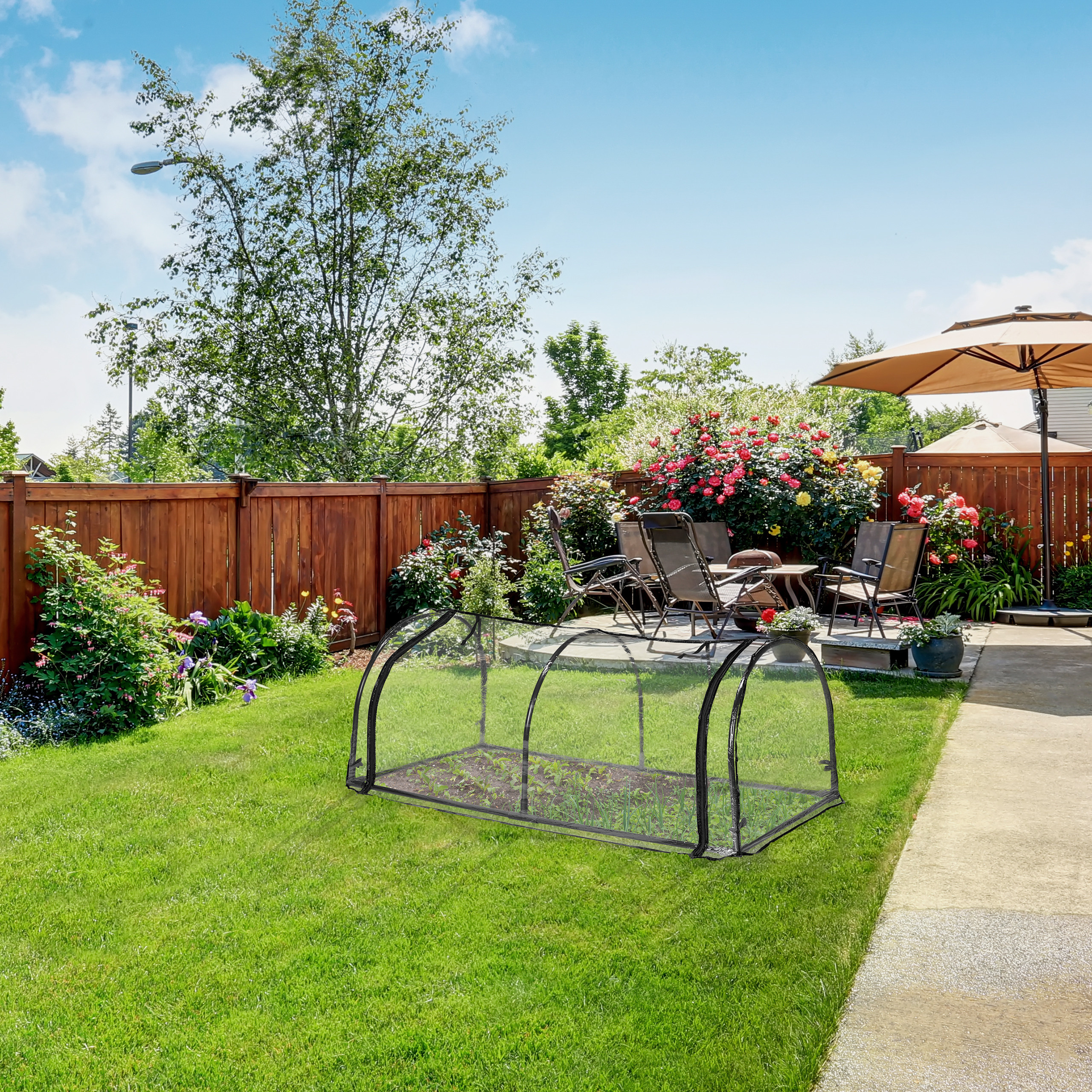 Ein sonniger Garten mit Rasen, einem kleinen Gewächshaus, Holzfences, Blumen und Gartenmöbeln mit Sonnenschirm.