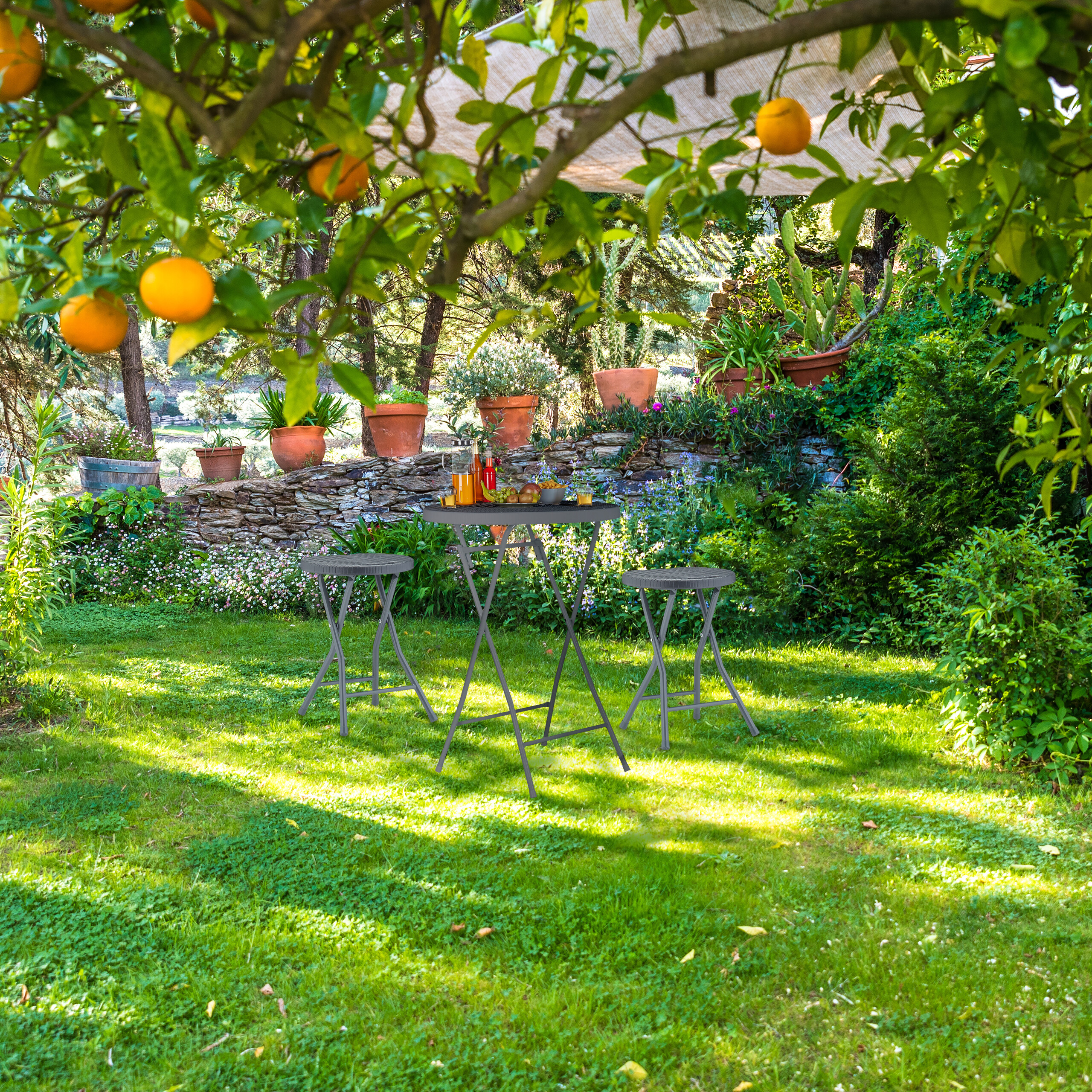 Ein Tisch mit Hockern im sonnigen Garten unter Orangenbäumen mit Steineinrichtung im Hintergrund.