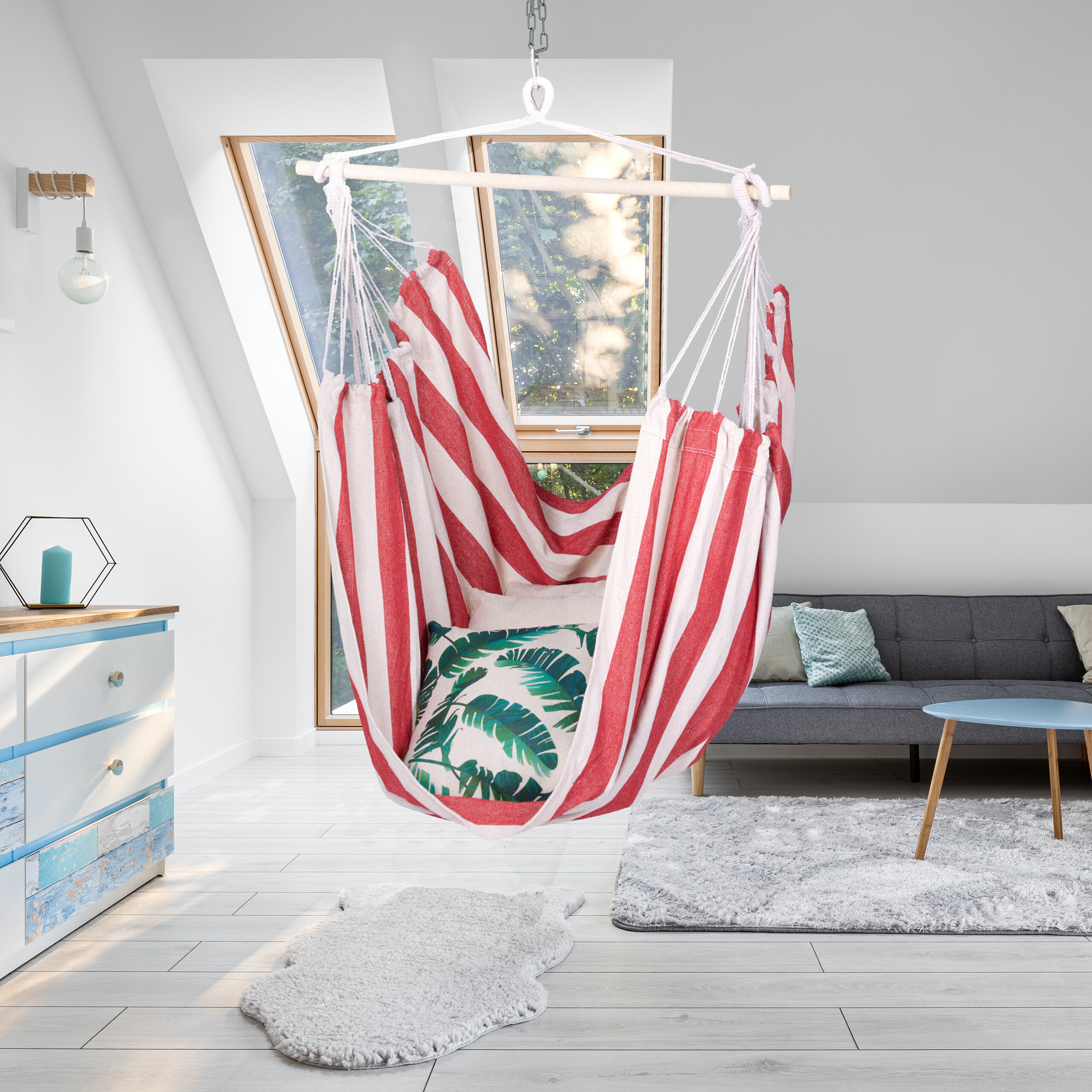 Ein rot-weiß gestreifter Hängesessel hängt in einem hellen, modernen Wohnzimmer mit Dachfenstern.