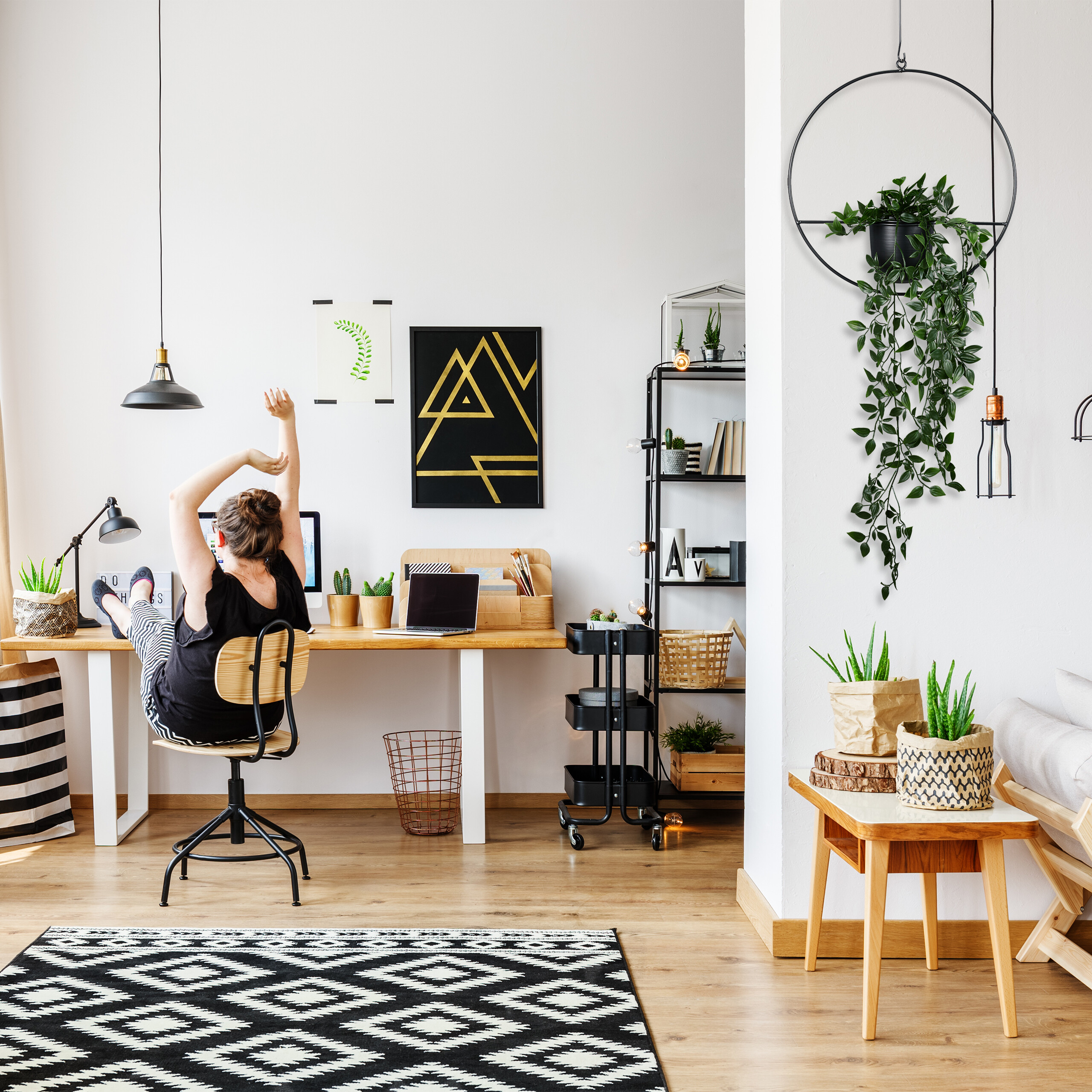 Eine Person sitzt in einem hellen Homeoffice und streckt sich vor einem Schreibtisch mit Laptop.