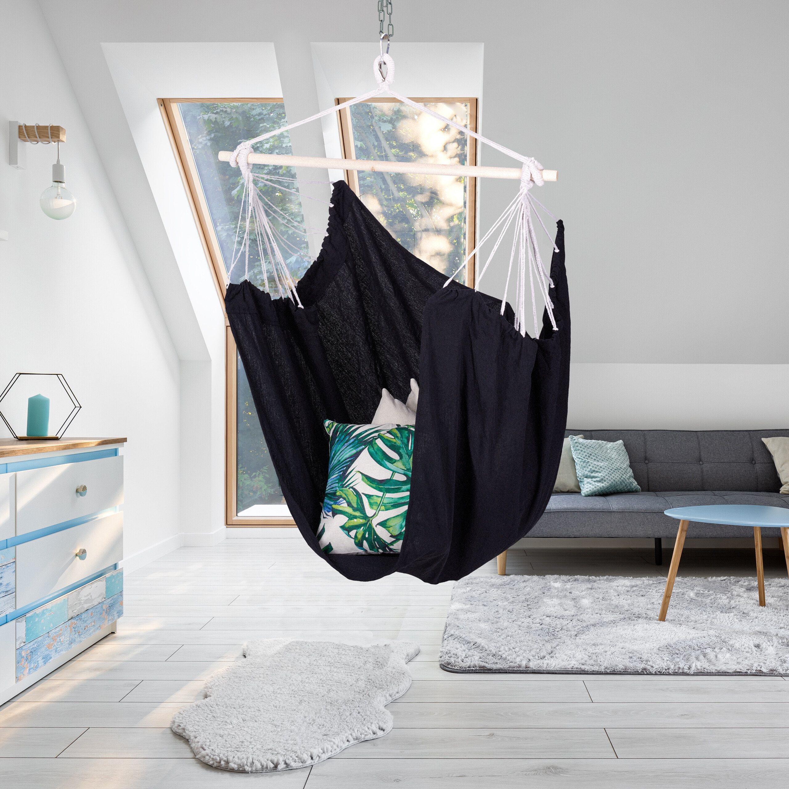 Ein schwarzer Hängesessel mit Kissen in einem modernen, hellen Raum mit Dachfenstern und einer Couch.