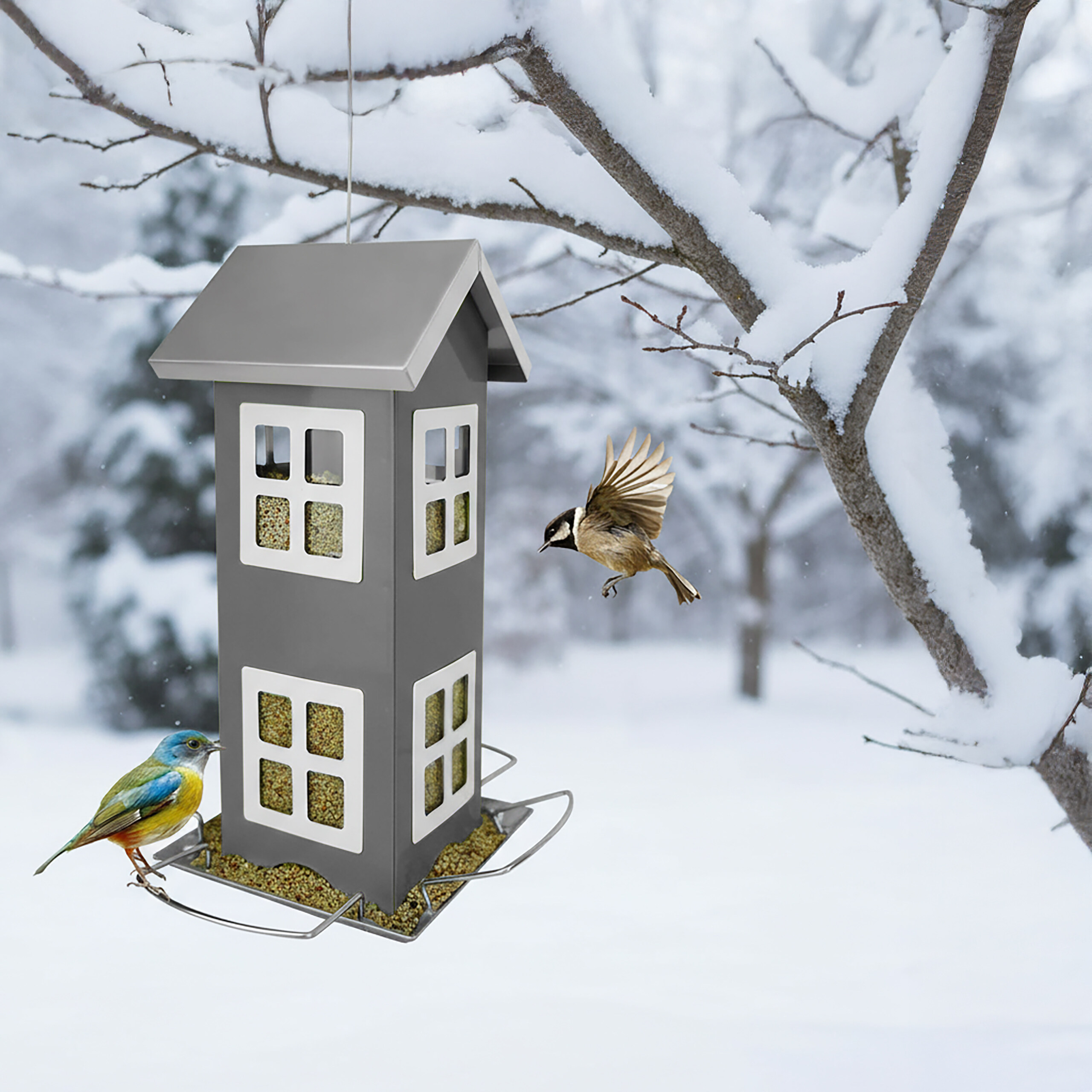 Ein graues, hausförmiges Vogelhäuschen im Schnee mit zwei kleinen Vögeln.
