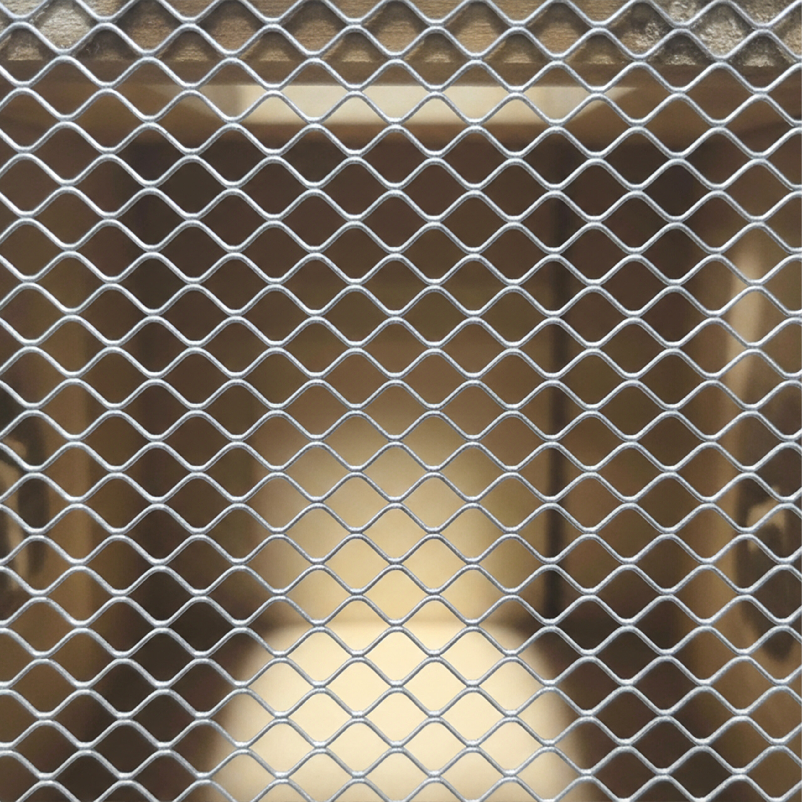 Ein silbernes Metallgitter mit rautenförmigen Maschen deckt einen hölzernen Innenraum ab.