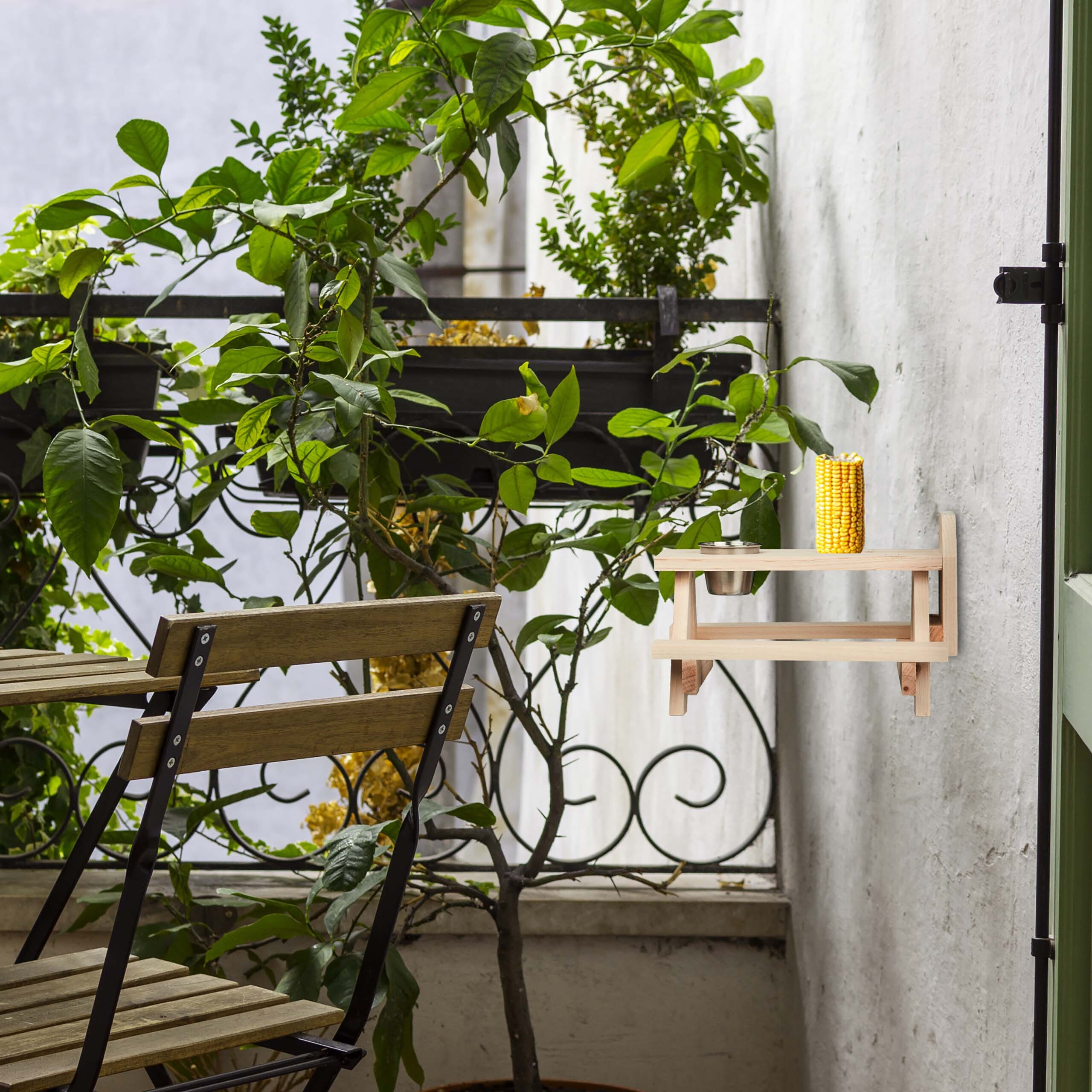 Ein kleiner Holztisch ist auf einem Balkon mit grünen Pflanzen an einer weißen Wand befestigt.