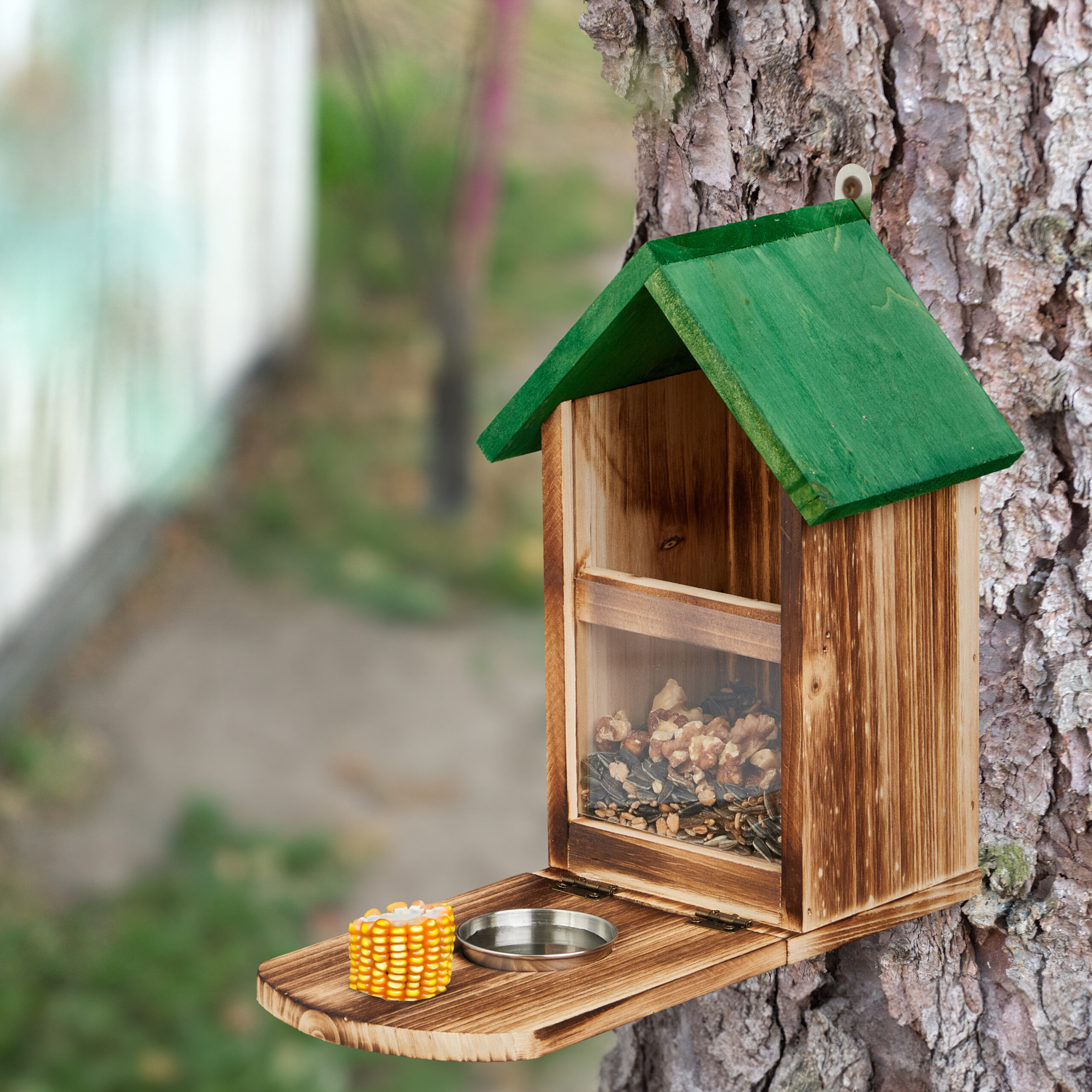 Ein hölzernes Vogelhäuschen mit grünem Dach und Futter ist an einem Baumstamm befestigt.