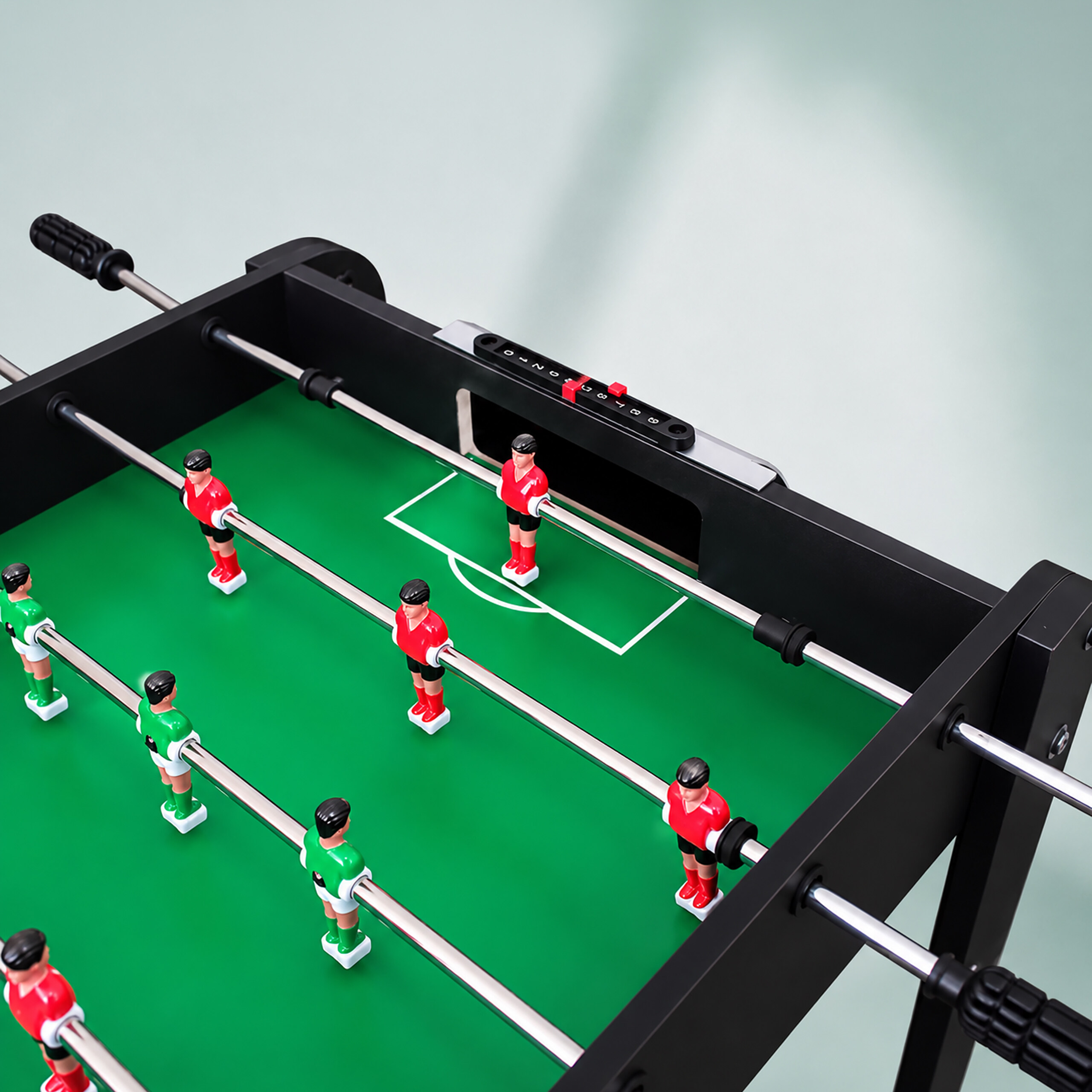 Ein Tischkicker mit grünem Spielfeld, schwarzen Wänden und rot-grünen Figuren auf Metallstangen.