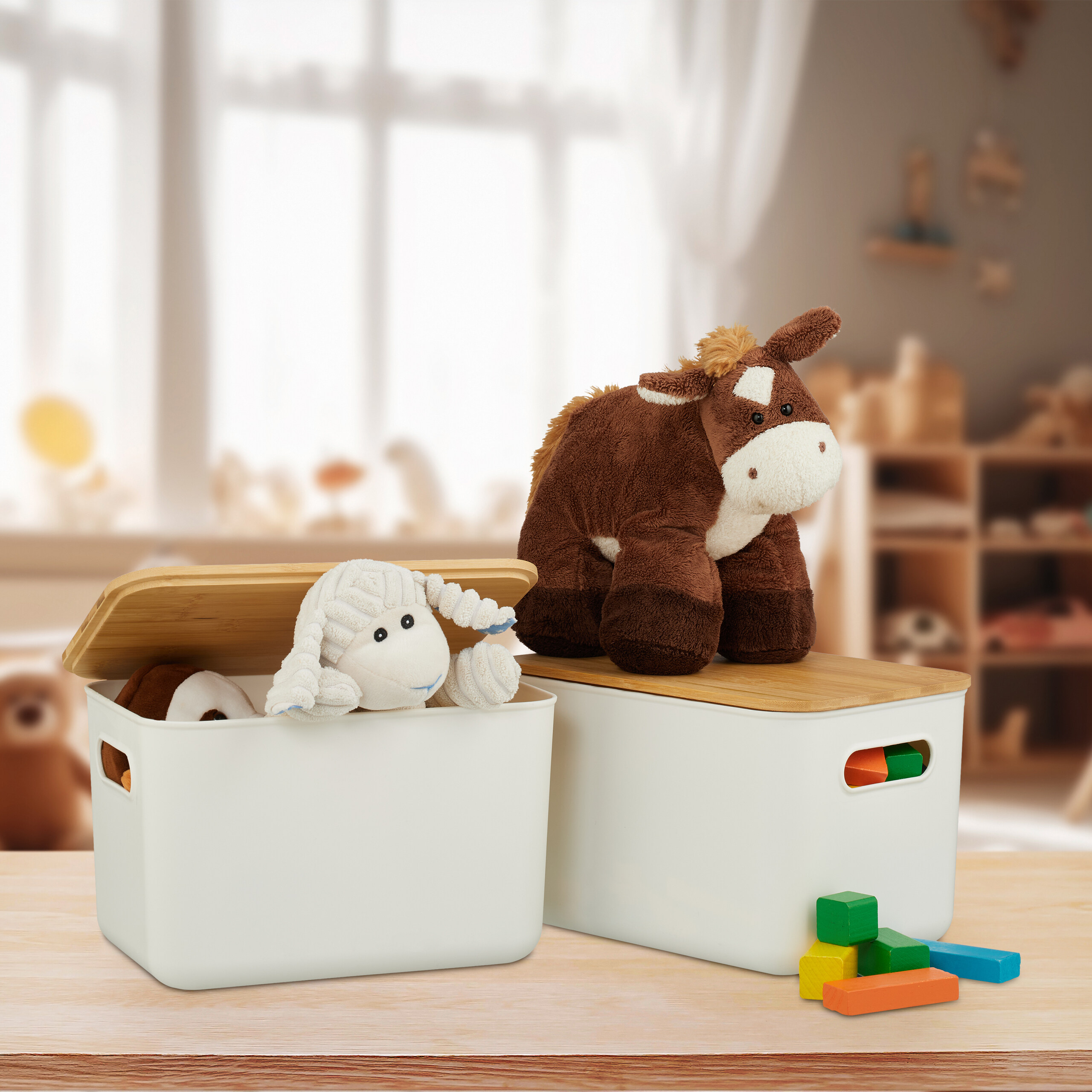 Zwei weiße Aufbewahrungsboxen mit Plüschtieren und Bauklötzen auf einem Holztisch.