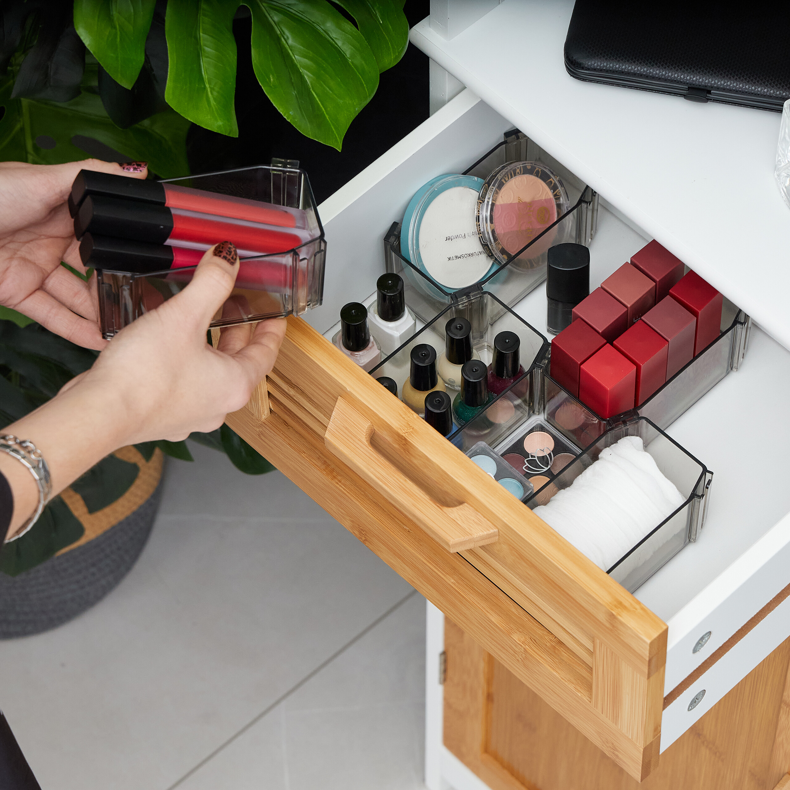 Eine Person hält einen klaren Behälter mit roten Lippenstiften über eine geöffnete Make-up-Schublade mit Kosmetika.