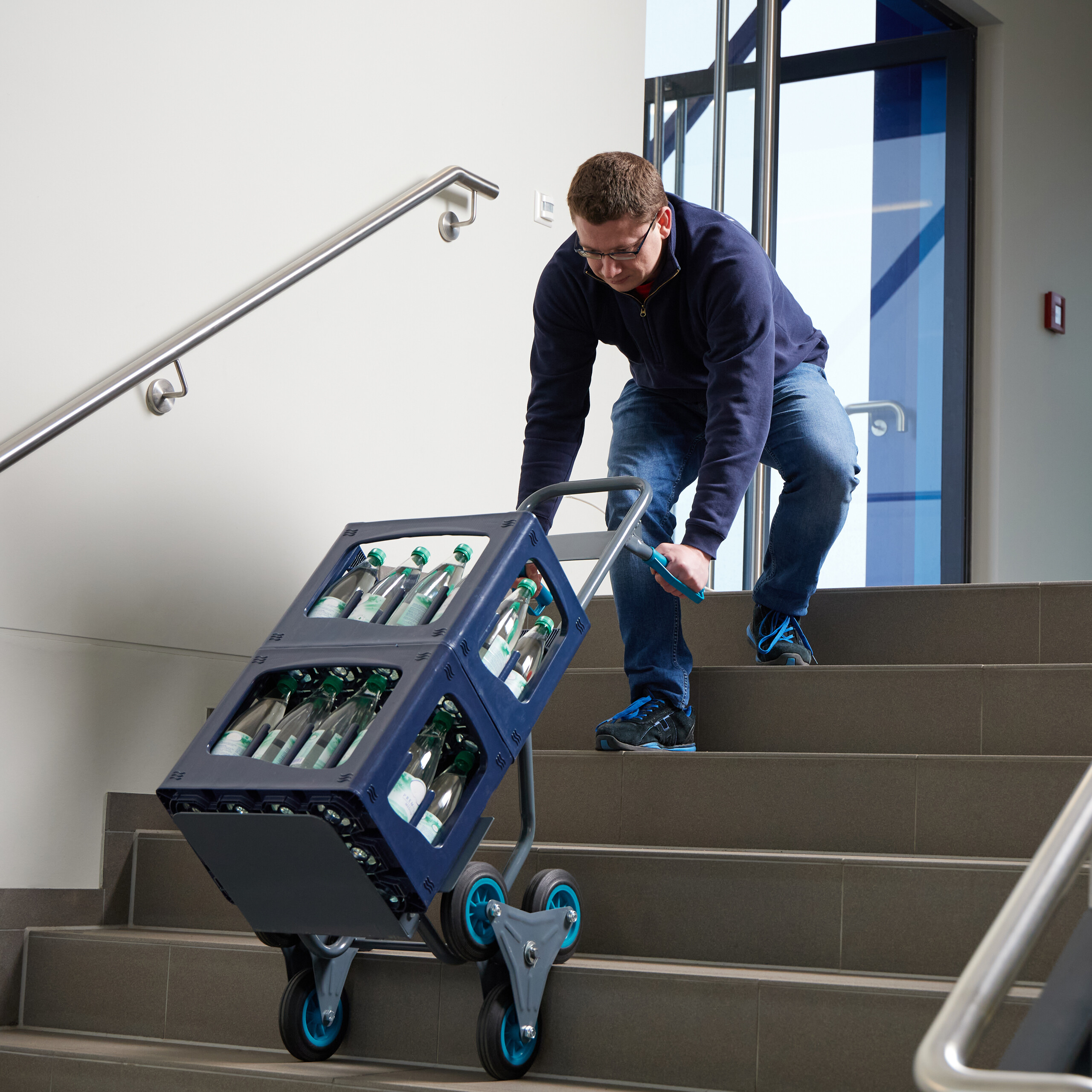 Ein Mann zieht eine Sackkarre mit Getränkekisten vorsichtig eine Treppe hinunter.