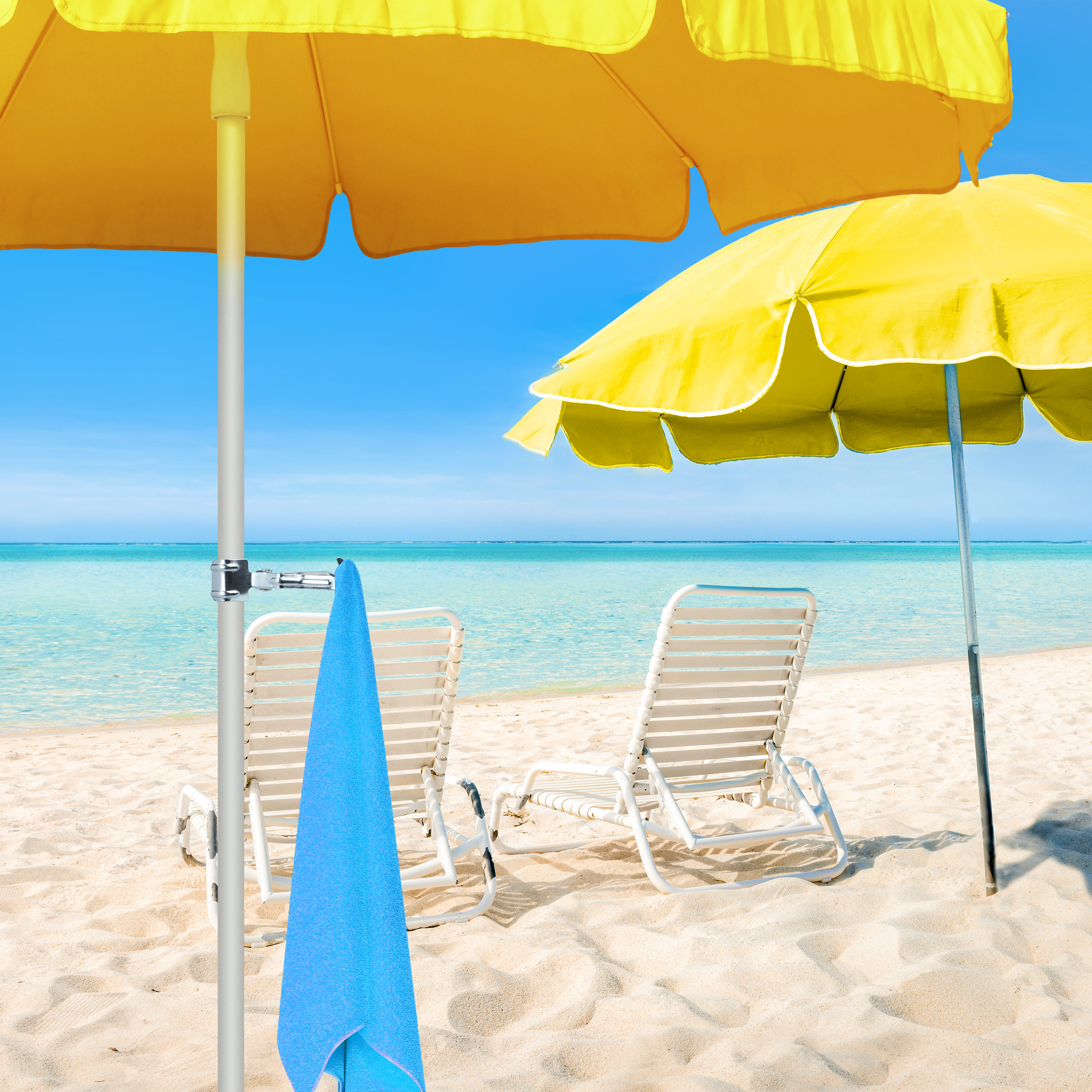 Zwei gelbe Sonnenschirme und Liegestühle am sandigen Strand mit klarem blauen Meer.