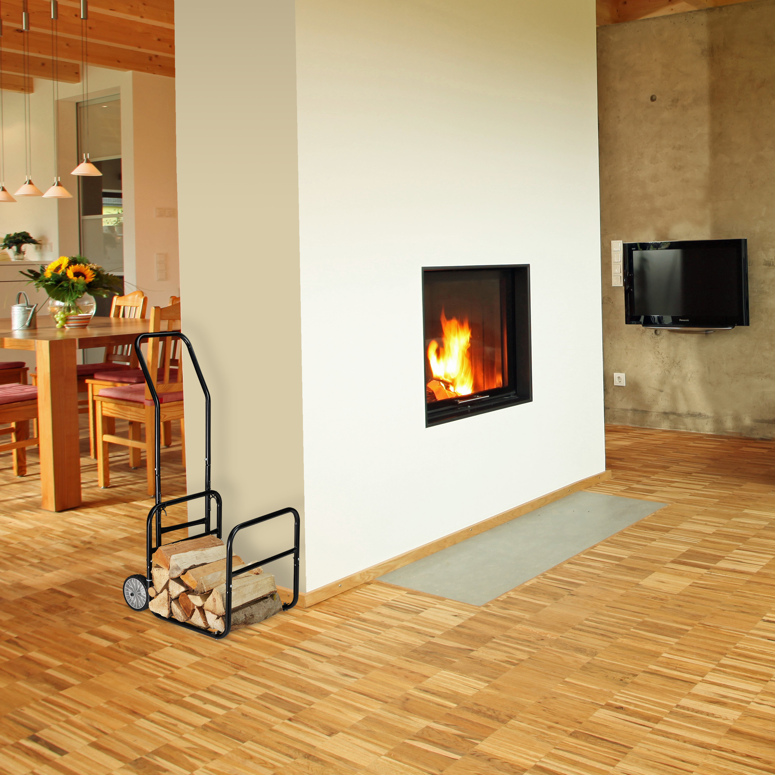 Ein Kamin in einer weißen Wand mit einem mit Holz gefüllten Metallwagen davor auf Holzboden.
