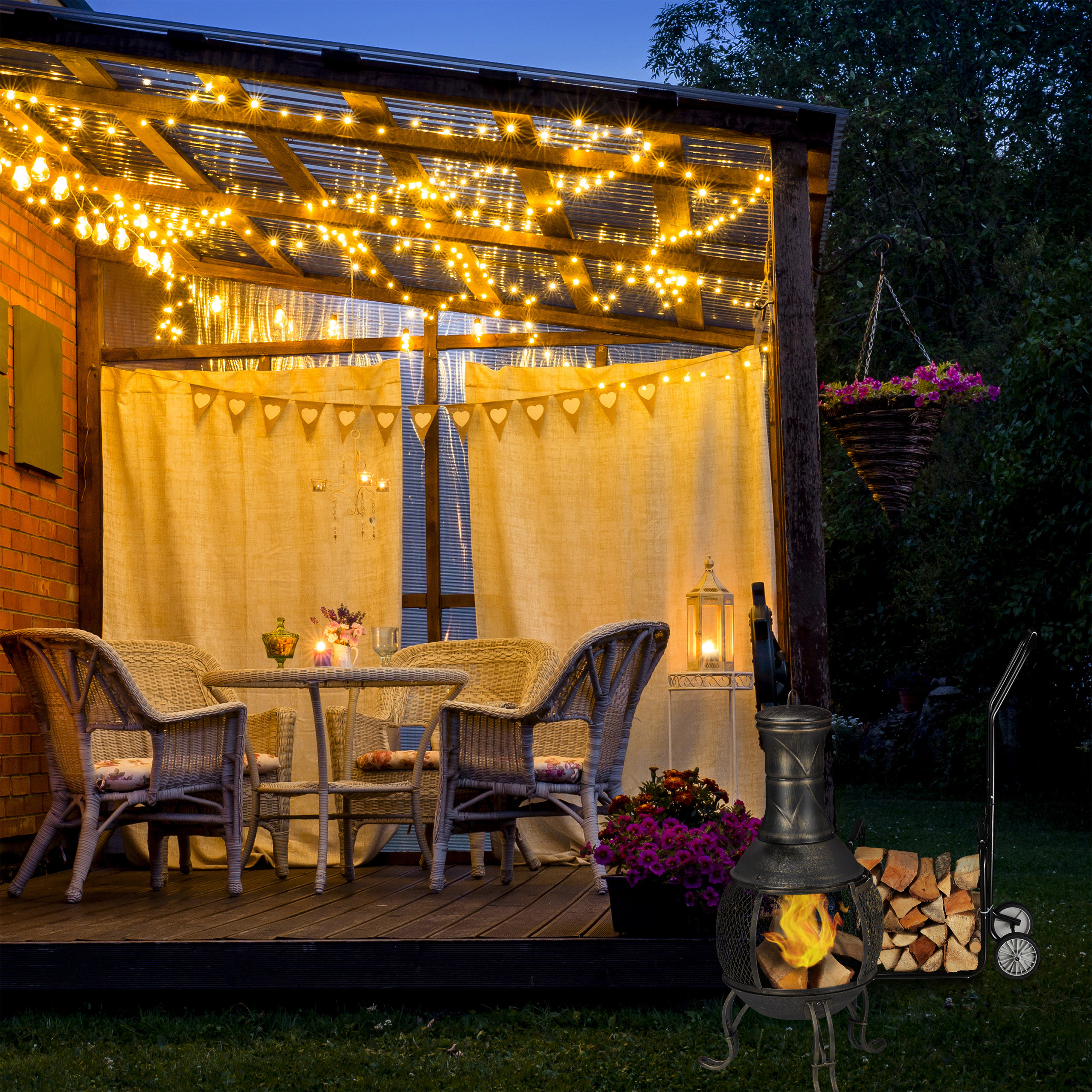 Gemütliche beleuchtete Terrasse bei Nacht mit Wicker-Möbeln, Vorhängen und einer Feuerstelle mit Holz.