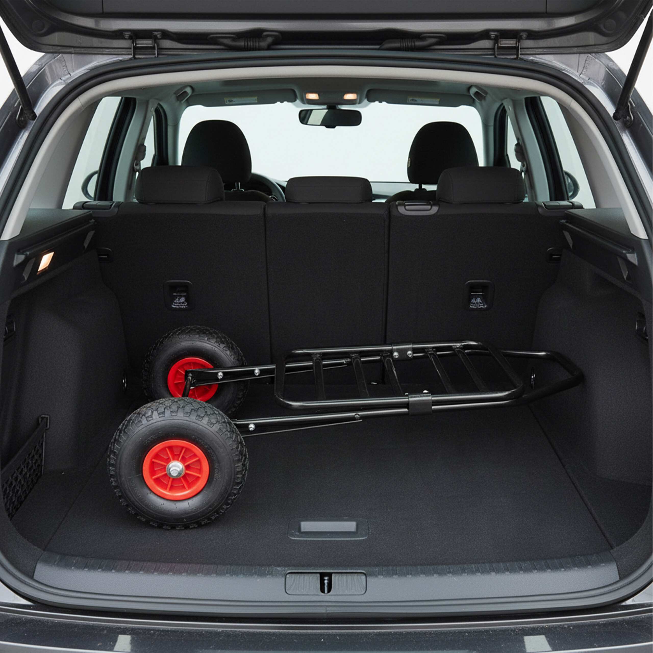 Eine zusammengeklappte schwarze Sackkarre mit roten Rädern liegt im Kofferraum eines Autos.