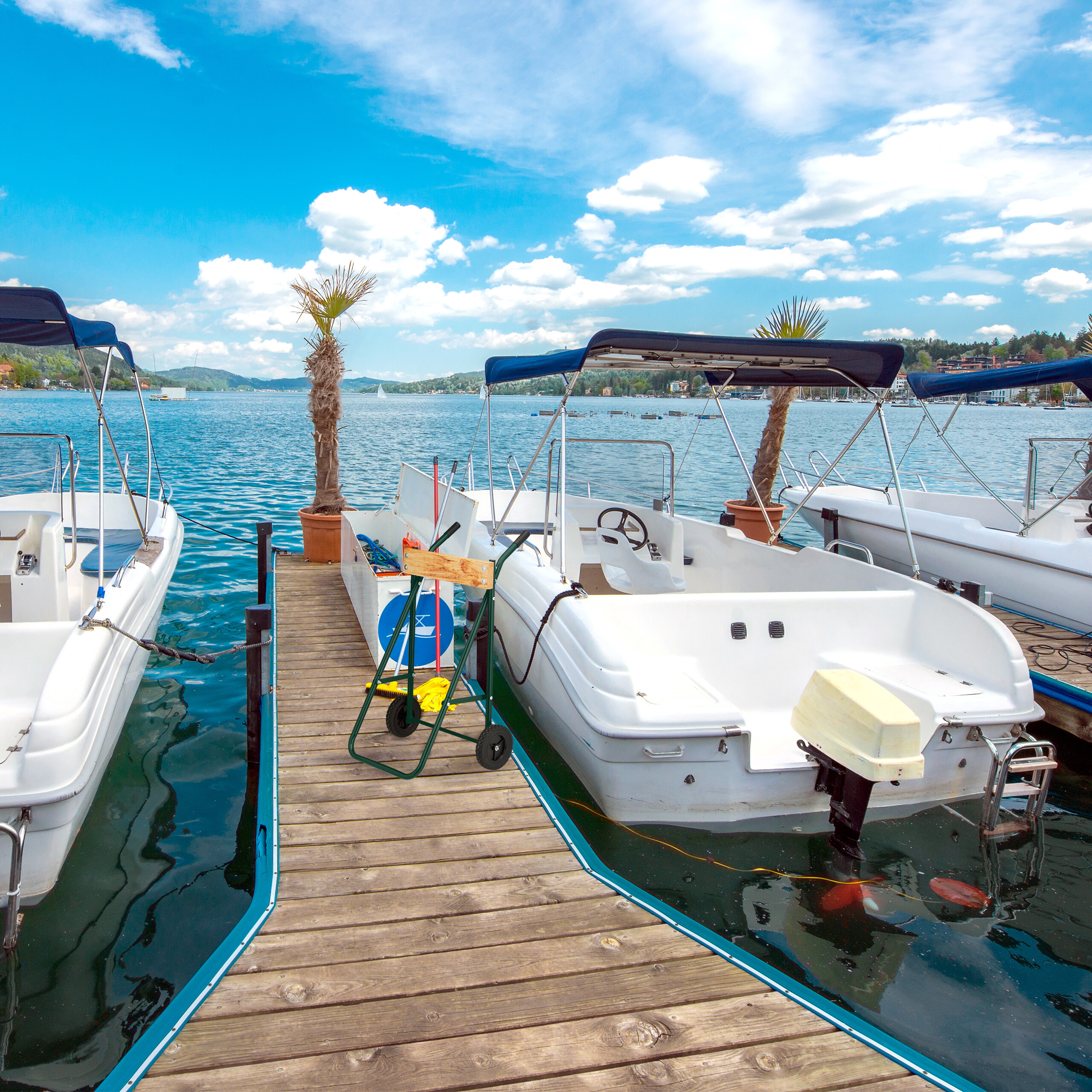 Weiße Motorboote liegen an einem Holzsteg im blauen See unter einem wolkenbedeckten Himmel.