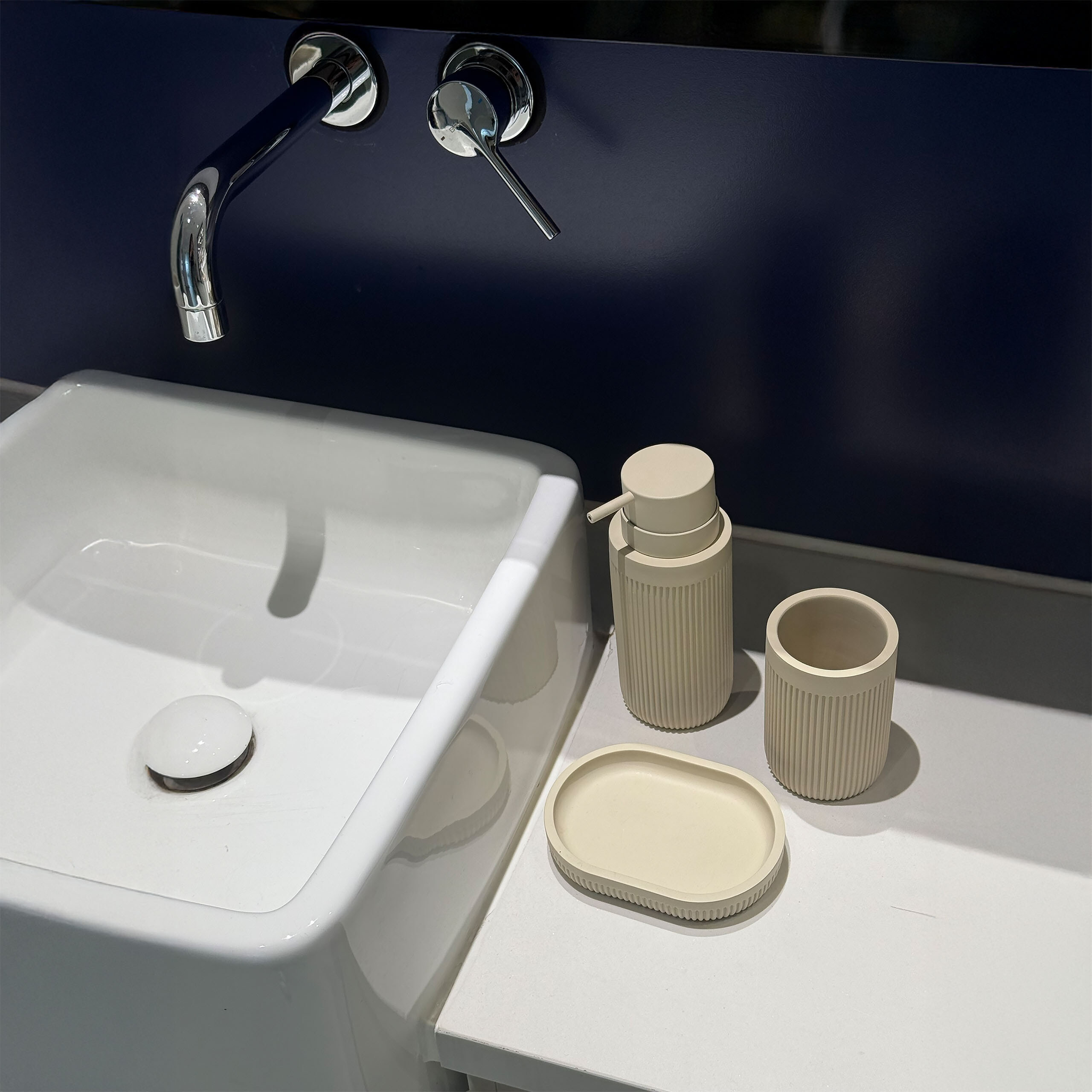 Ein weißes Waschbecken mit Chromarmatur und beigen Badezimmeraccessoires auf der Ablage.