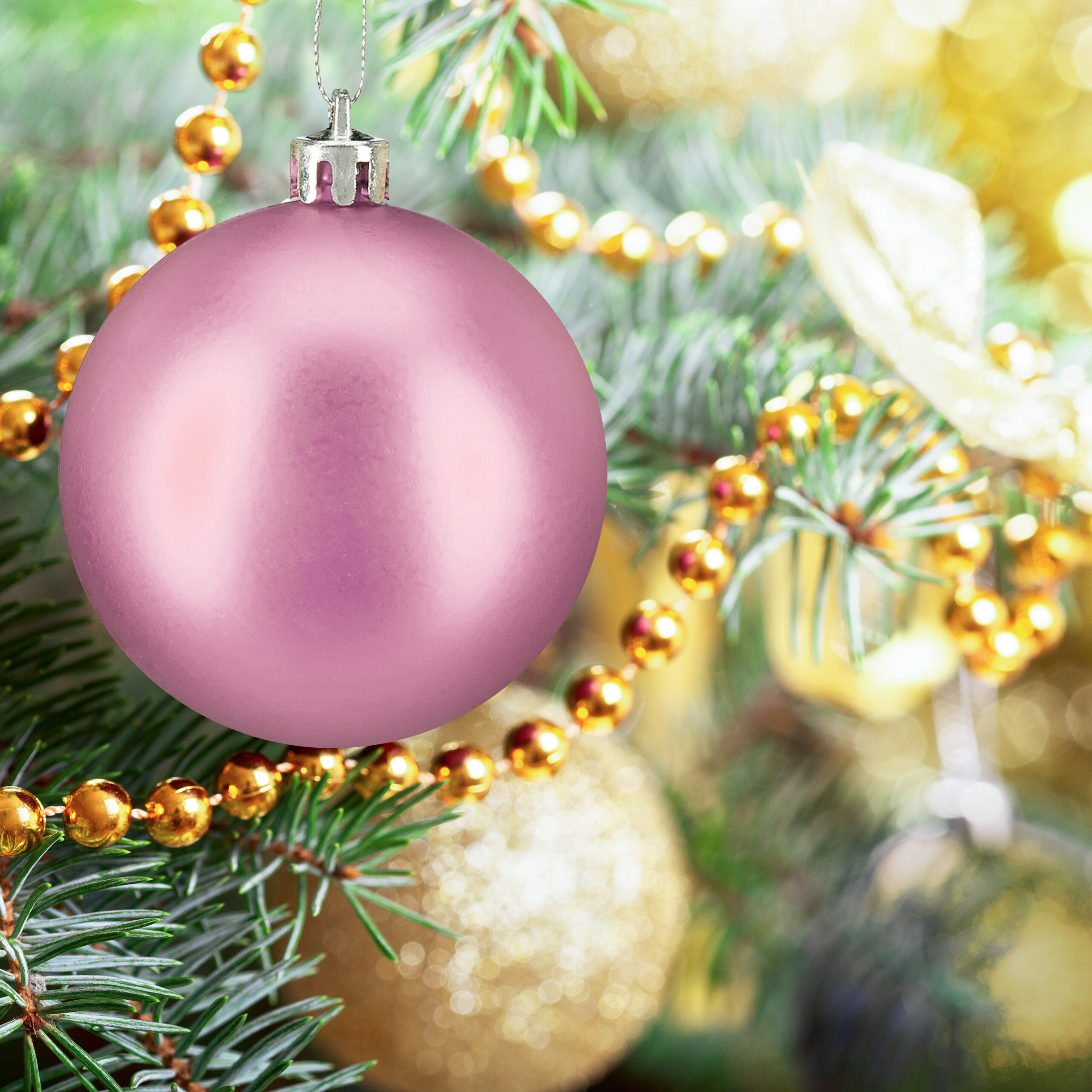 Eine matte rosa Weihnachtskugel hängt an einem grünen Zweig, umgeben von goldenen Perlen.