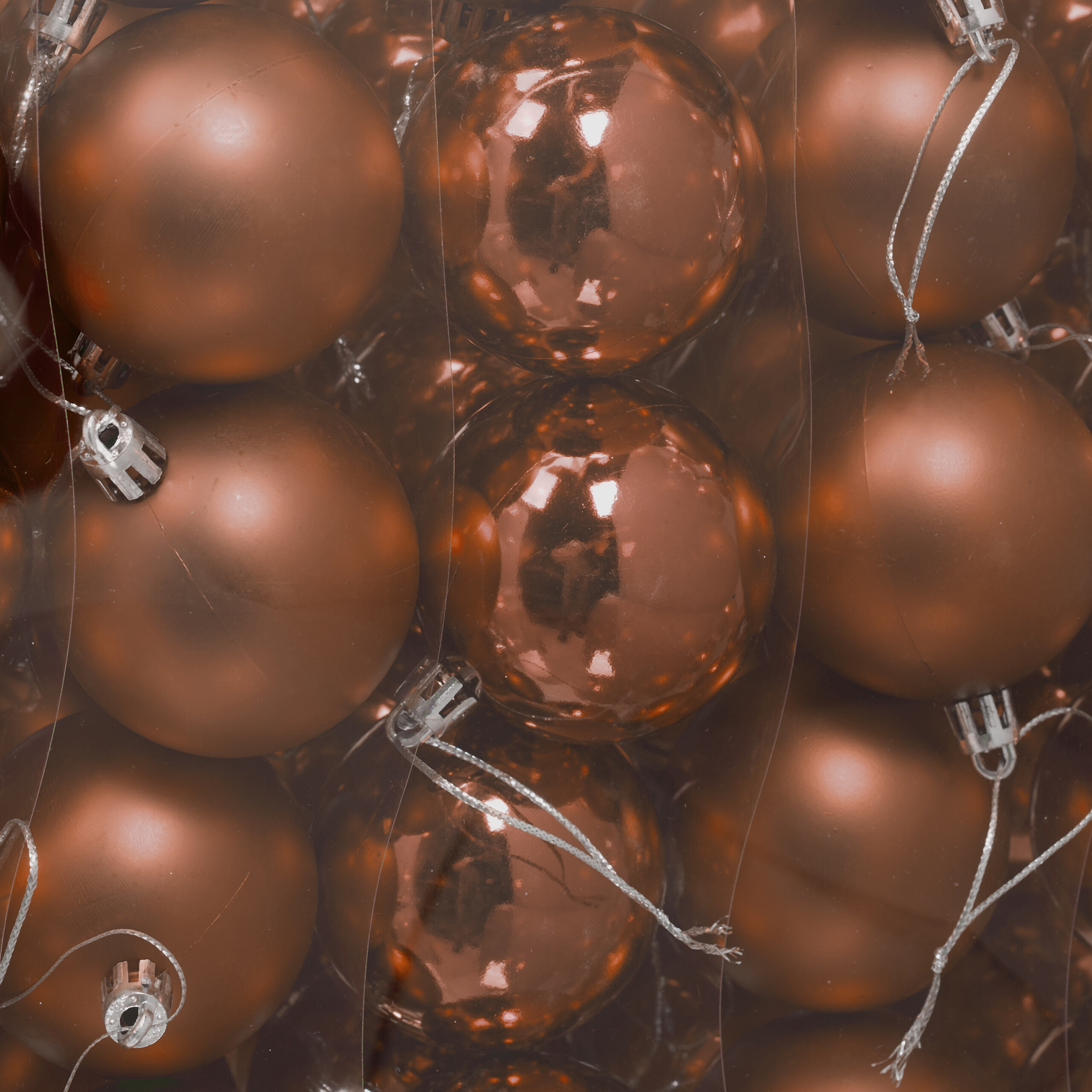Nahaufnahme glänzender und matter kupferfarbener Christbaumkugeln, dicht in einer transparenten Plastikbox verpackt.