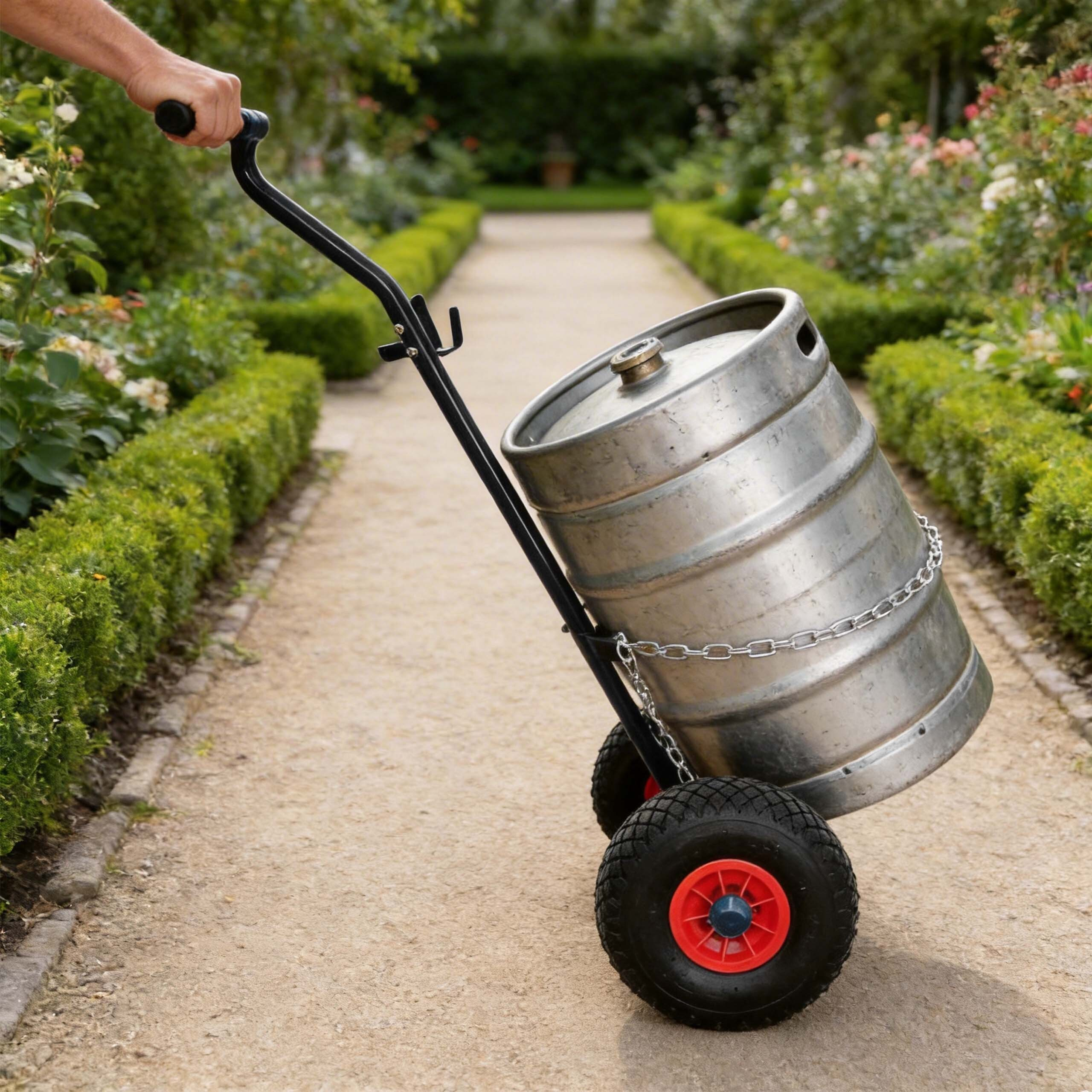 Ein Metallbierfass wird auf einem Handwagen auf einem Gartenweg transportiert.