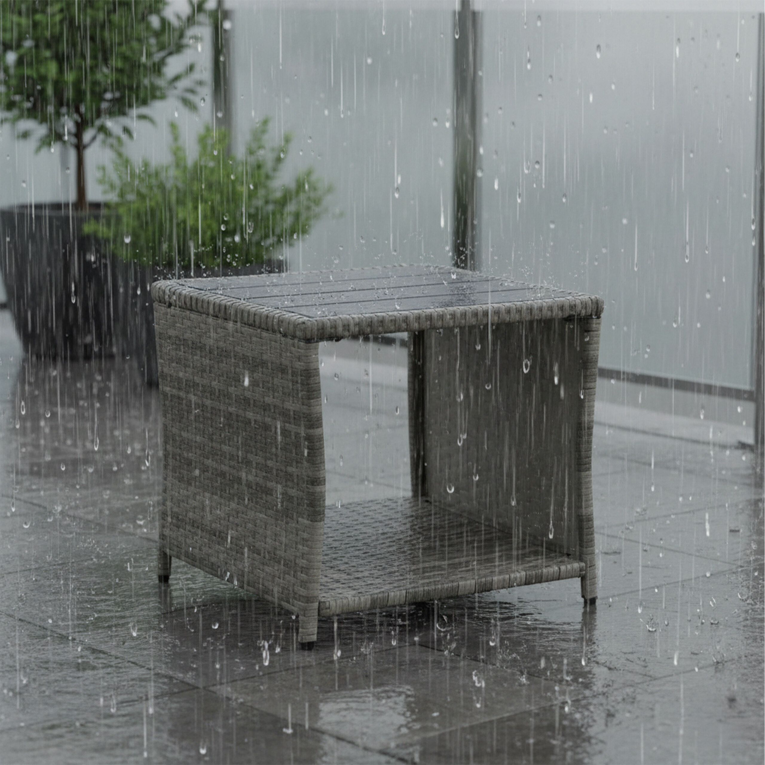Ein grauer Rattan-Beistelltisch auf einer gefliesten Terrasse bei starkem Regen.