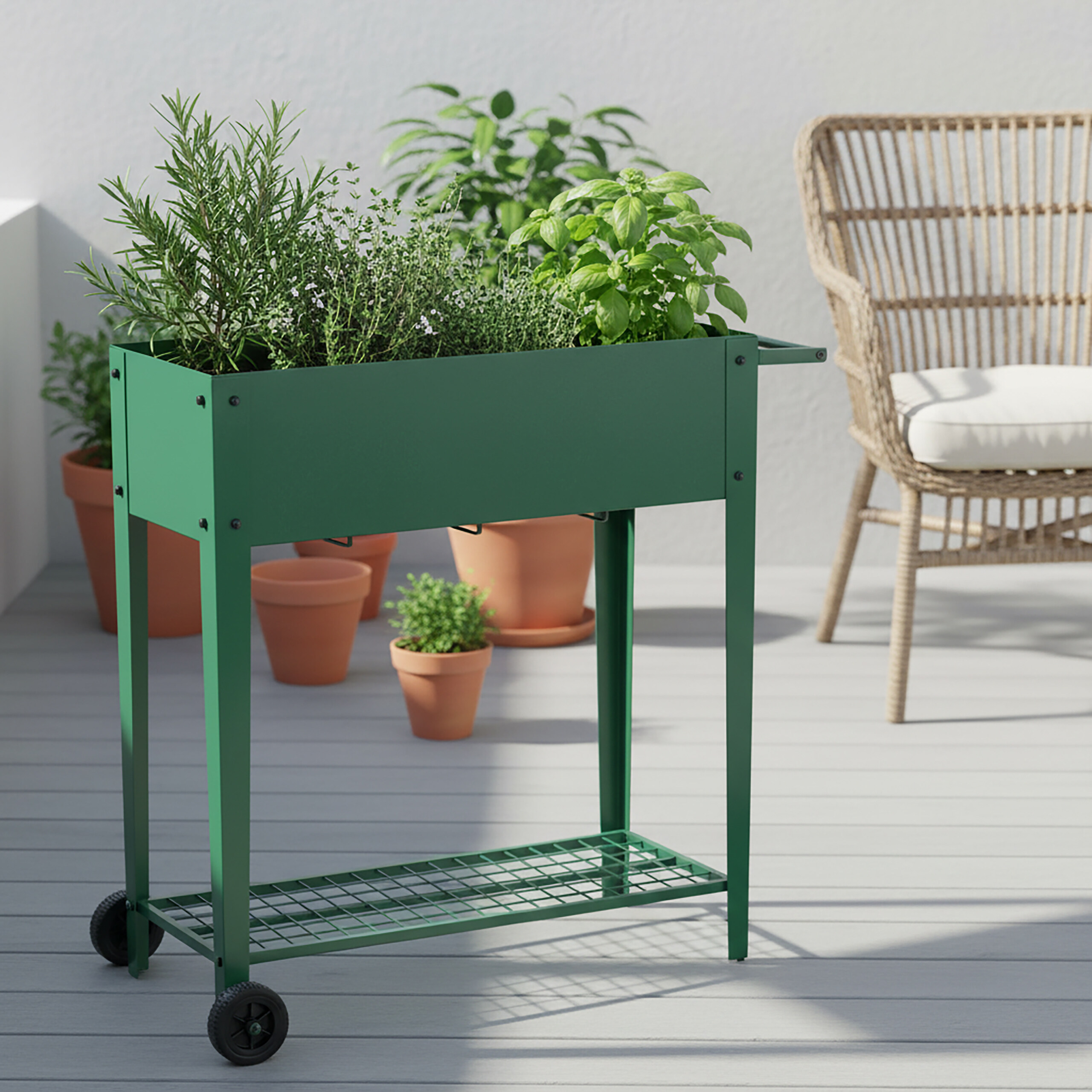 Ein grüner Pflanzenwagen mit Kräutern, Terrakottatöpfen und einem Korbstuhl auf einer Terrasse.