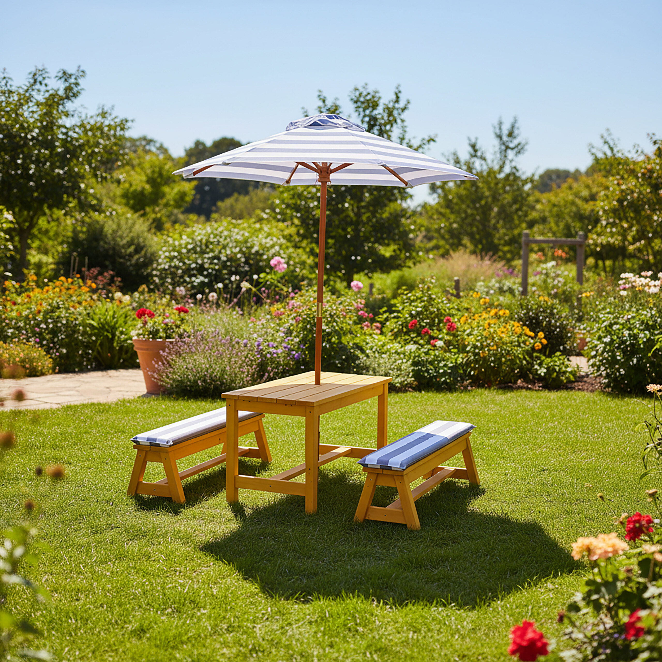 Ein hölzerner Picknicktisch mit Bänken und blau-weiß gestreiftem Sonnenschirm auf einem grünen Rasen im Garten.
