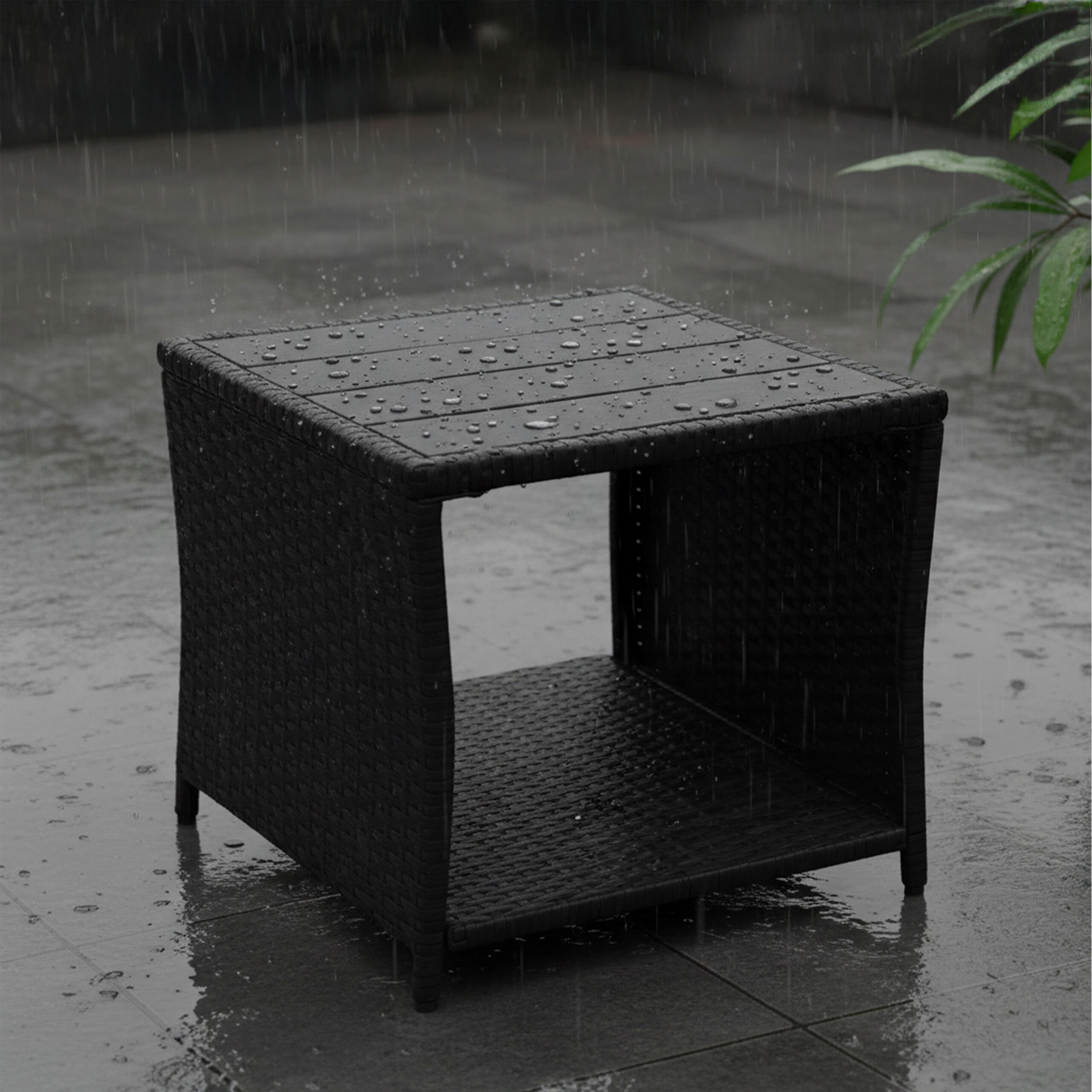 Ein schwarzer Rattan-Beistelltisch steht im Regen auf einer nassen Terrasse, mit Wassertropfen auf der Oberfläche.