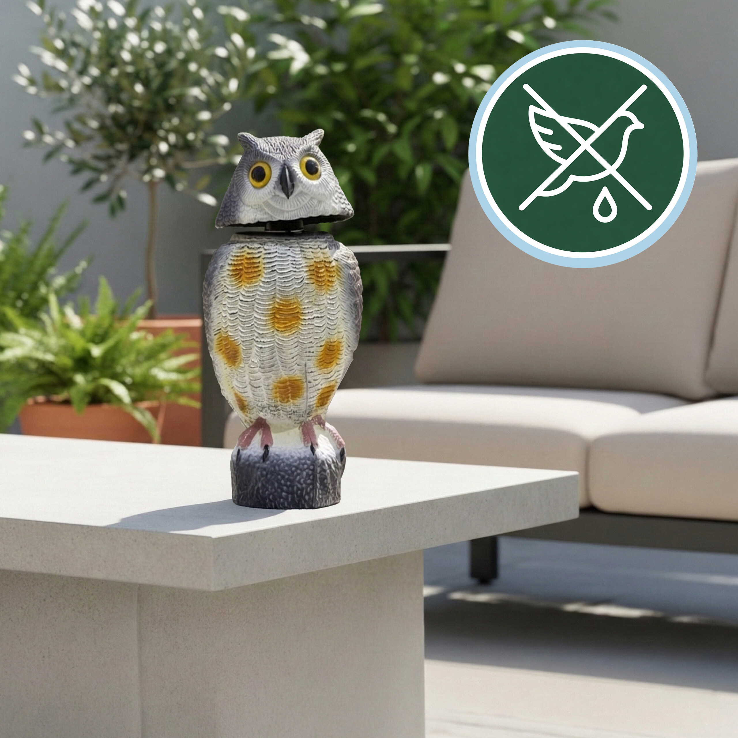 Eine Eulen-Gartenfigur steht auf einem Tisch im Freien, dahinter ein Sofa und Pflanzen.