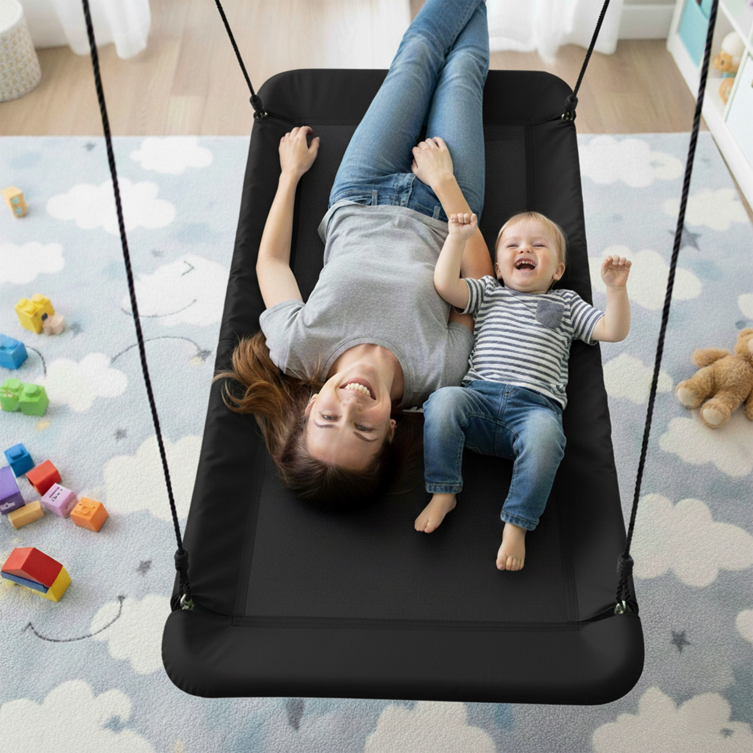 Eine glückliche Mutter und ihr kleiner Sohn liegen auf einer großen schwarzen Schaukel in einem Kinderzimmer.