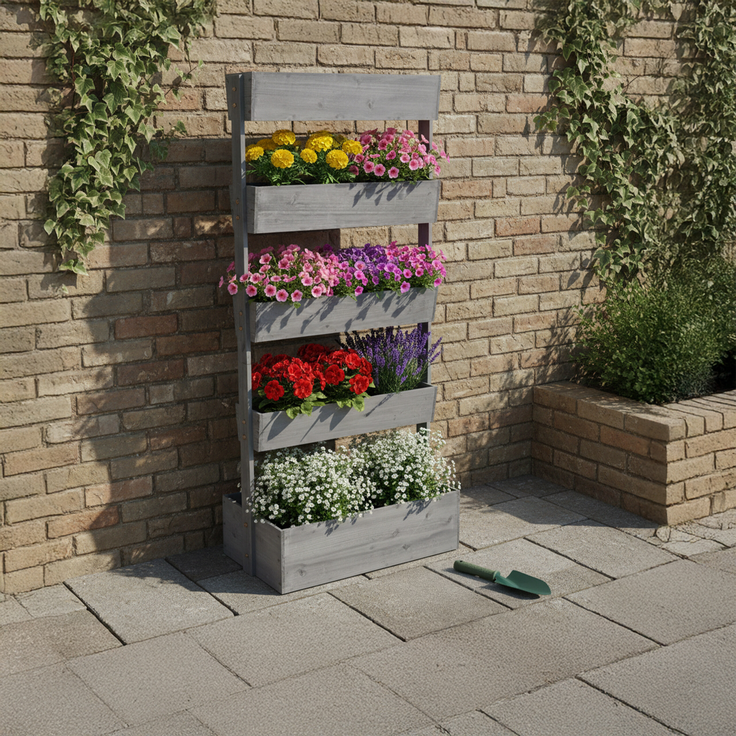 Ein grauer Holz-Vertikalpflanzer mit bunten Blumen steht auf gepflastertem Boden vor einer Ziegelwand.