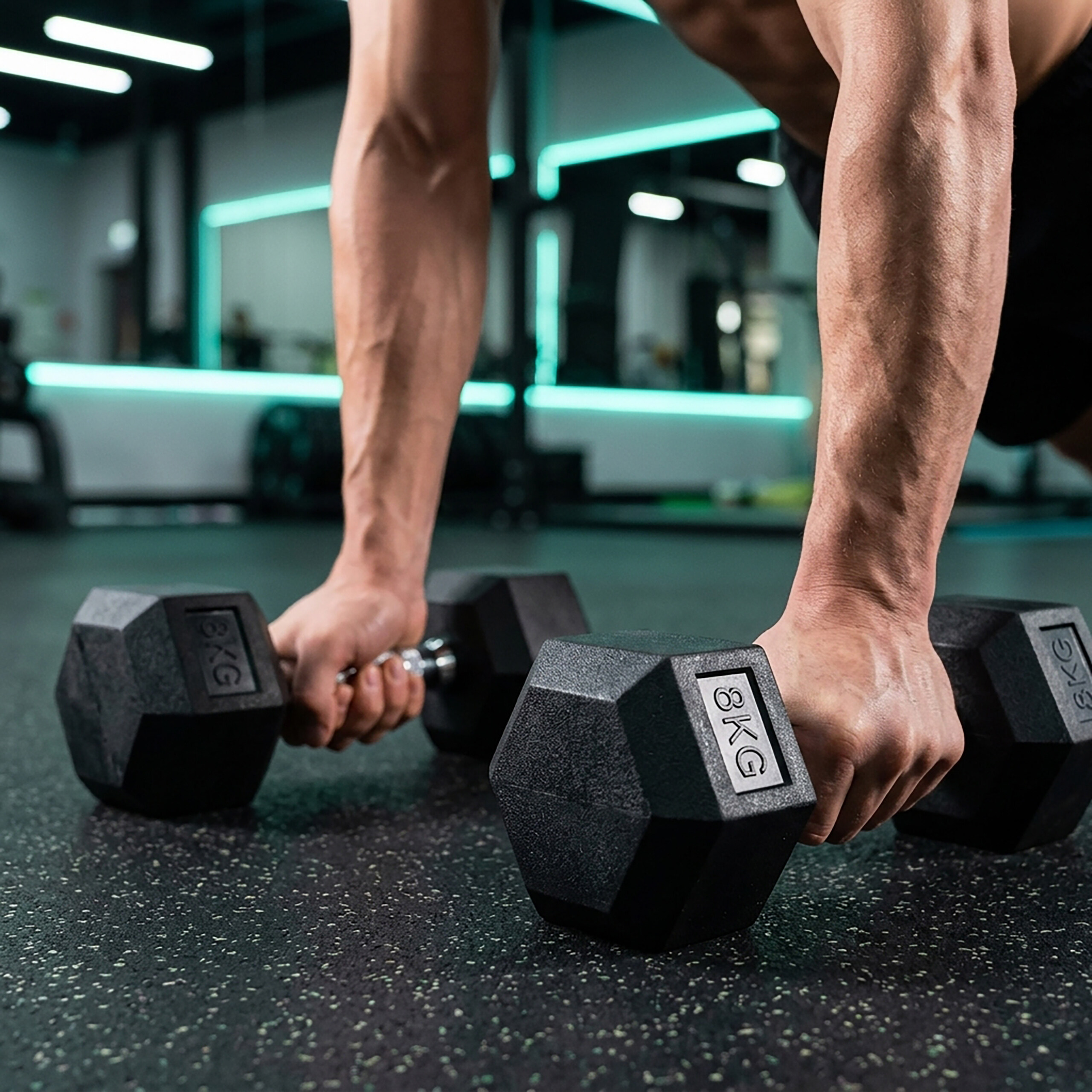 Muskulöser Mann macht Liegestütze auf zwei 8kg-Hanteln im Fitnessstudio.