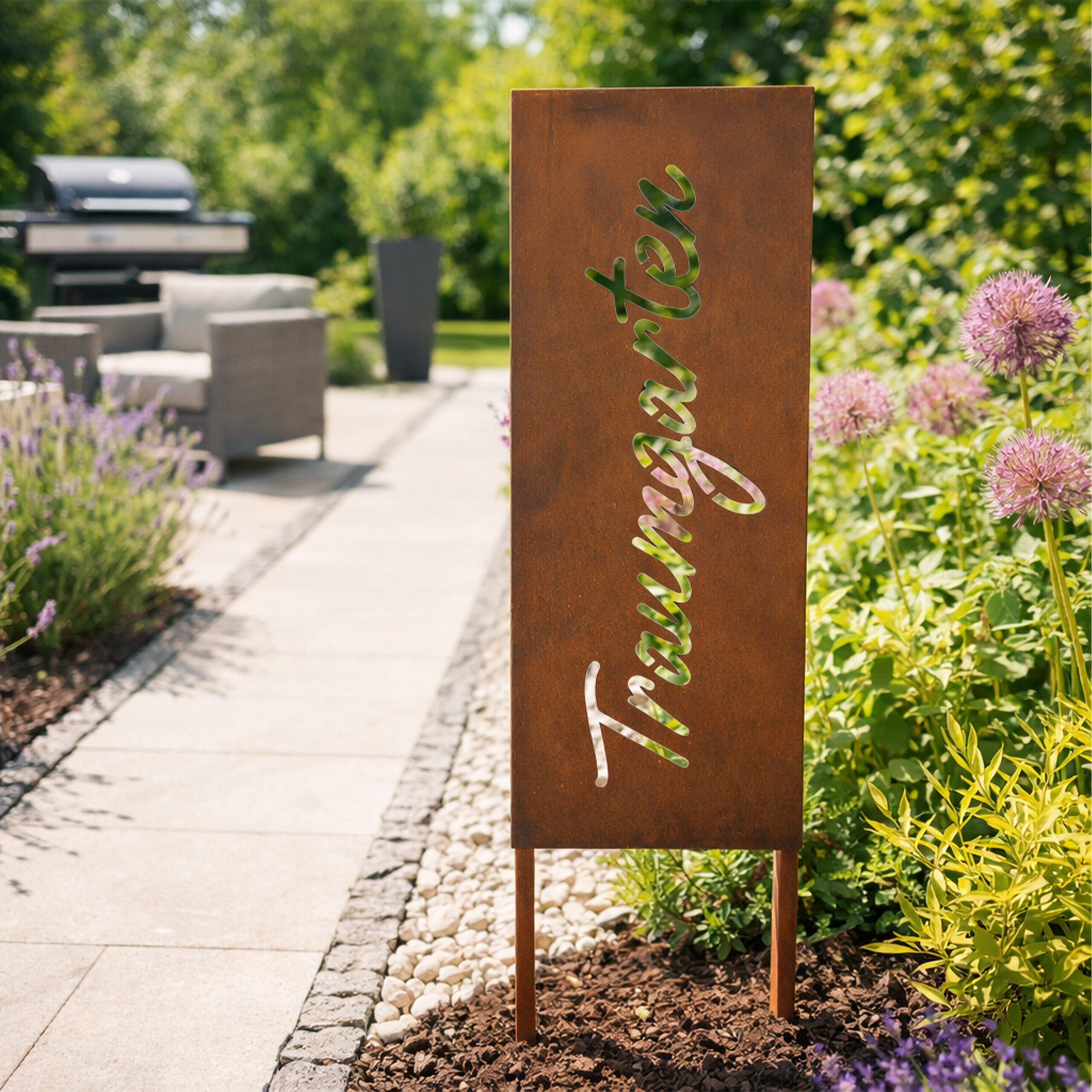 Rostfarbene Metalltafel mit dem Schriftzug "Traumgarten" steht im Garten neben einem Weg und Blumen.
