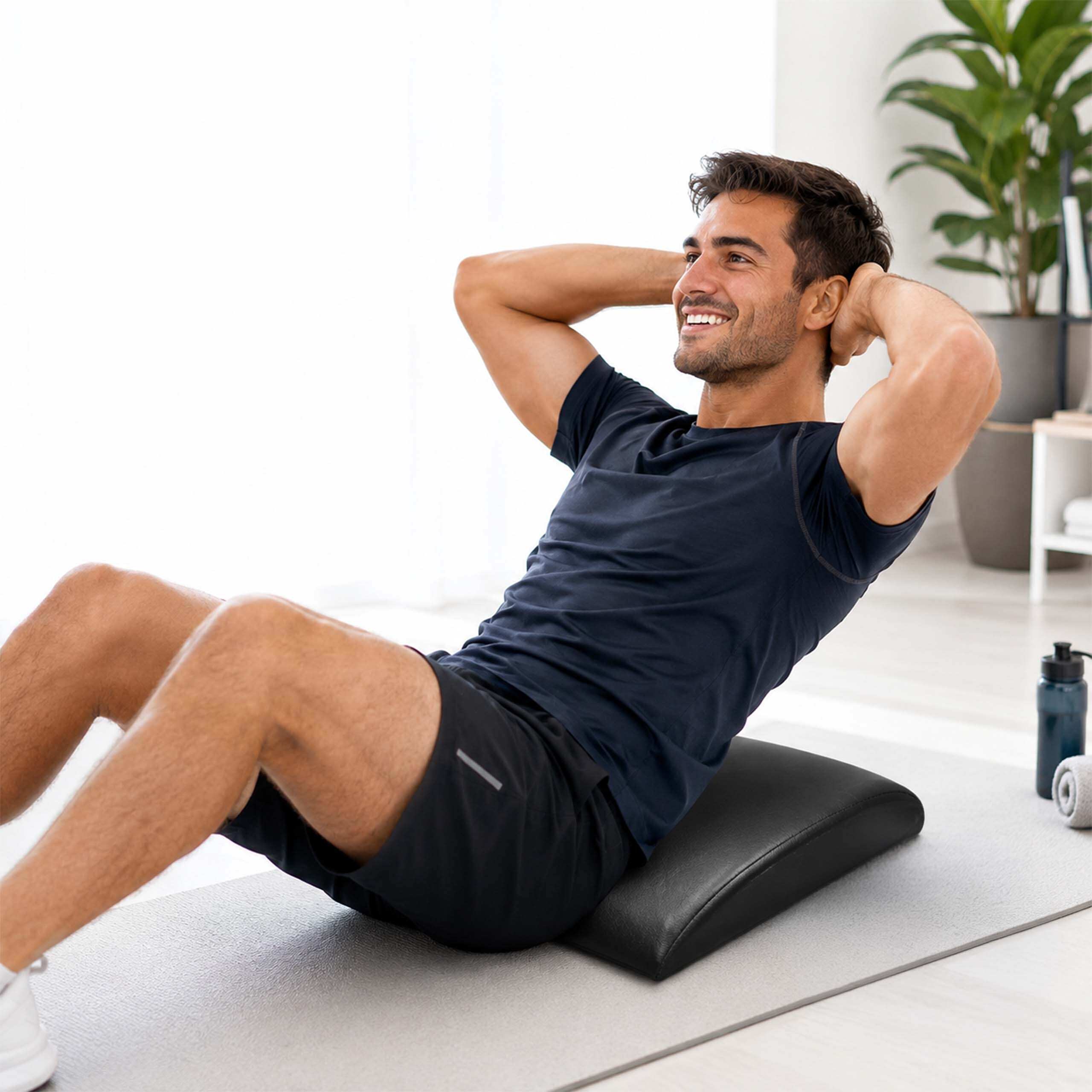 Ein lächelnder Mann in schwarzer Sportkleidung macht auf einer Matte in einem hellen Raum Sit-ups.